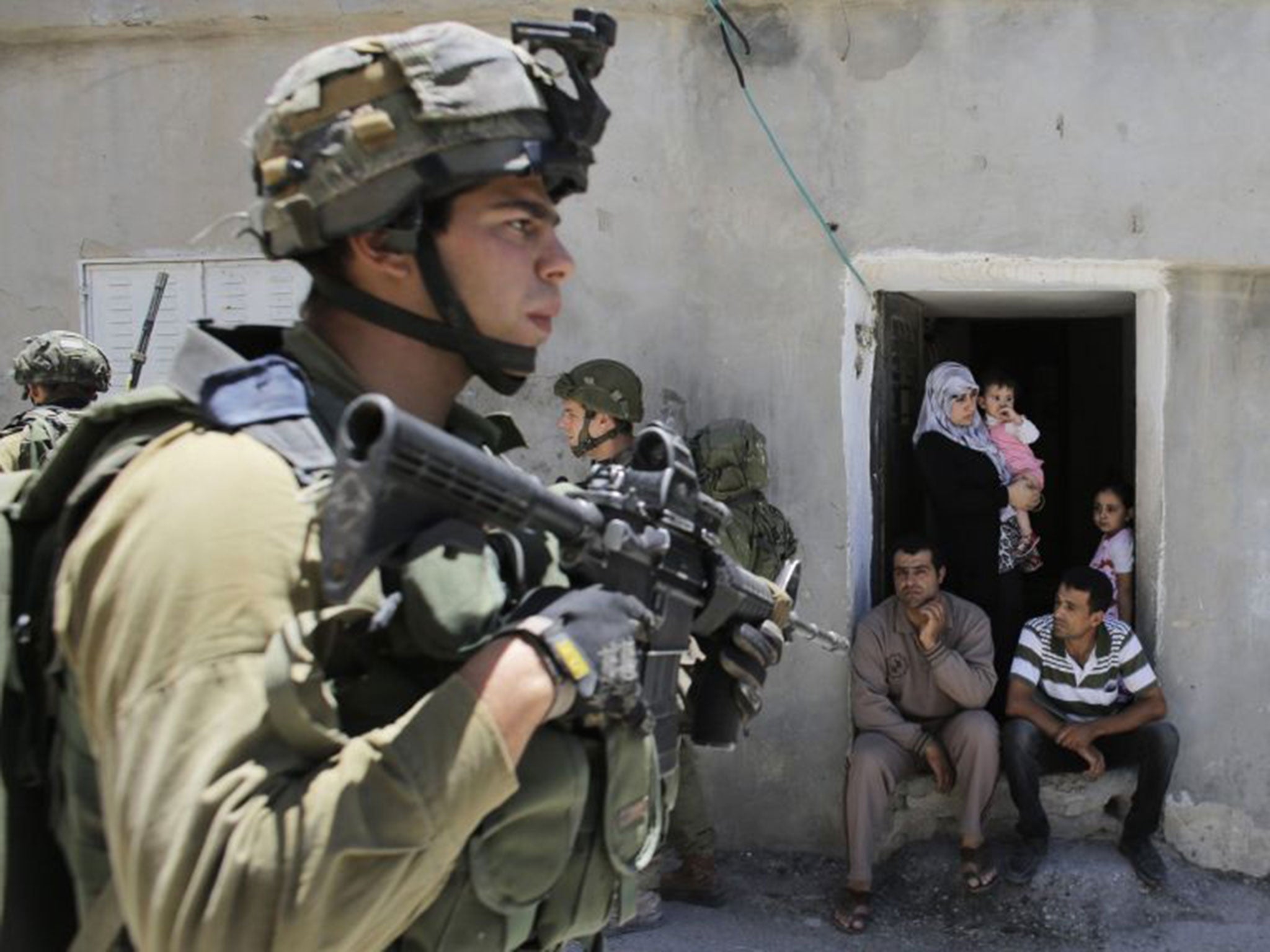 Palestinians watch Israeli soldiers patrol near the West Bank City of Hebron yesterday, close to where the teenagers were last seen