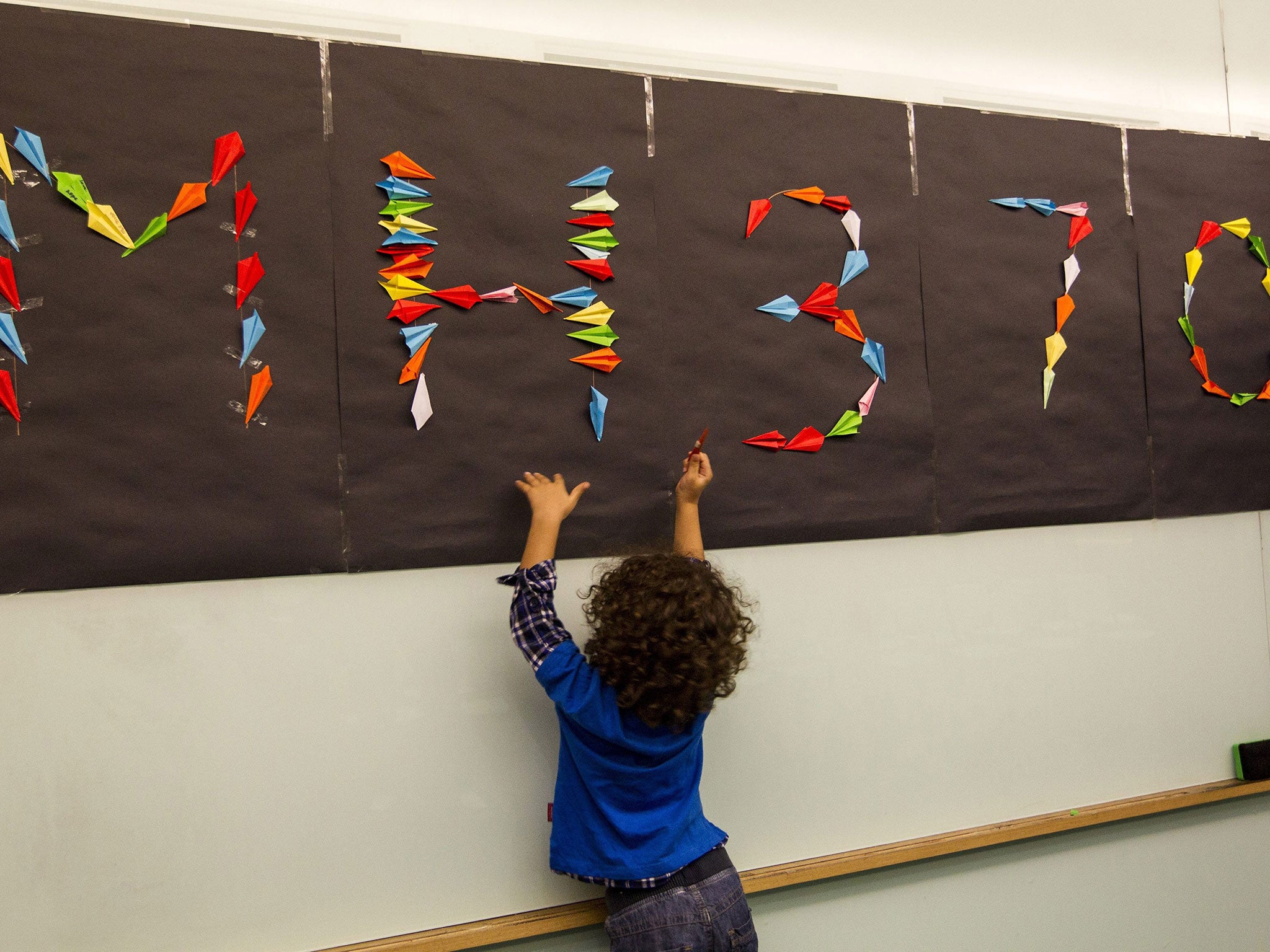 A young relative tries to stick paper planes on a board during an event to remember the 100th day of the missing crews and passengers of Malaysian Airlines plane MH370 in Damansara, Selangor