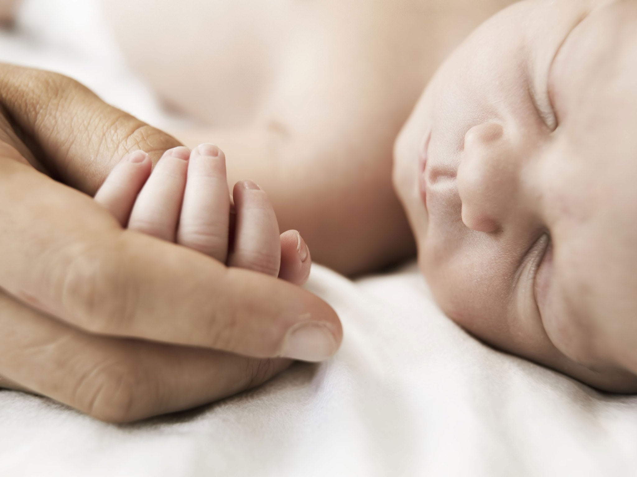 A mother holds the hand of her sleeping newborn son