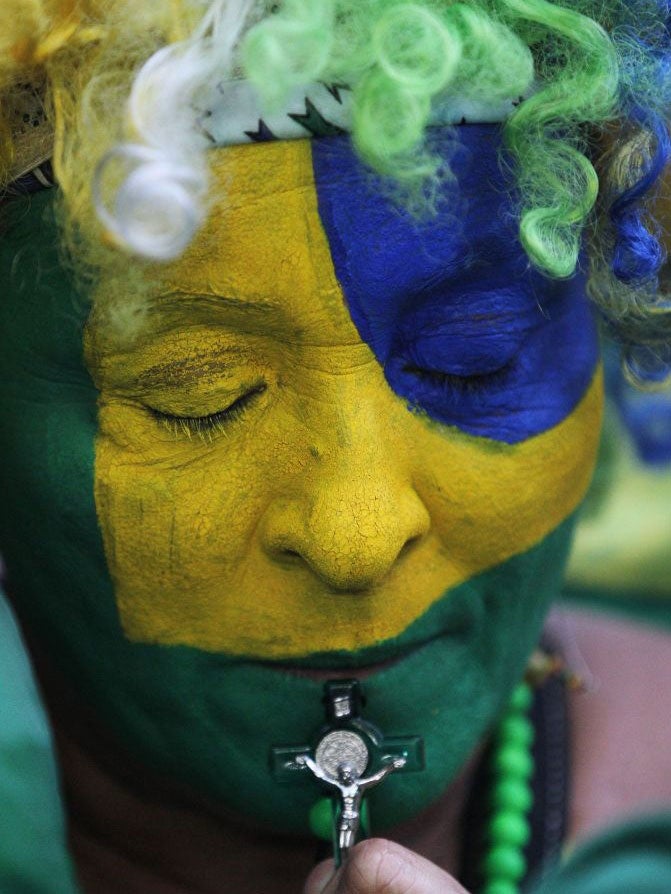 A Brazil fan, her face painted with the national colors, holds a crucifix, as she watches her team lose the World Cup semi-final against Germany (AP)