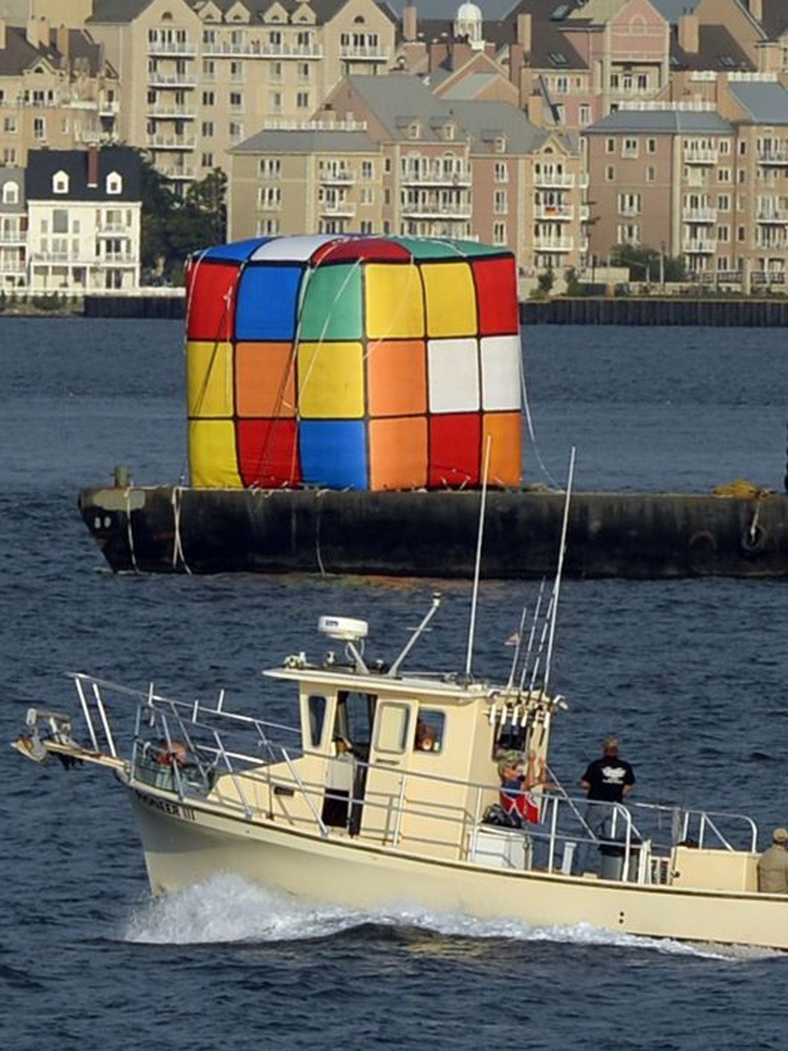 A tugboat tows a giant inflatable likeness of a Rubik's Cube puzzle near the Statue of Liberty