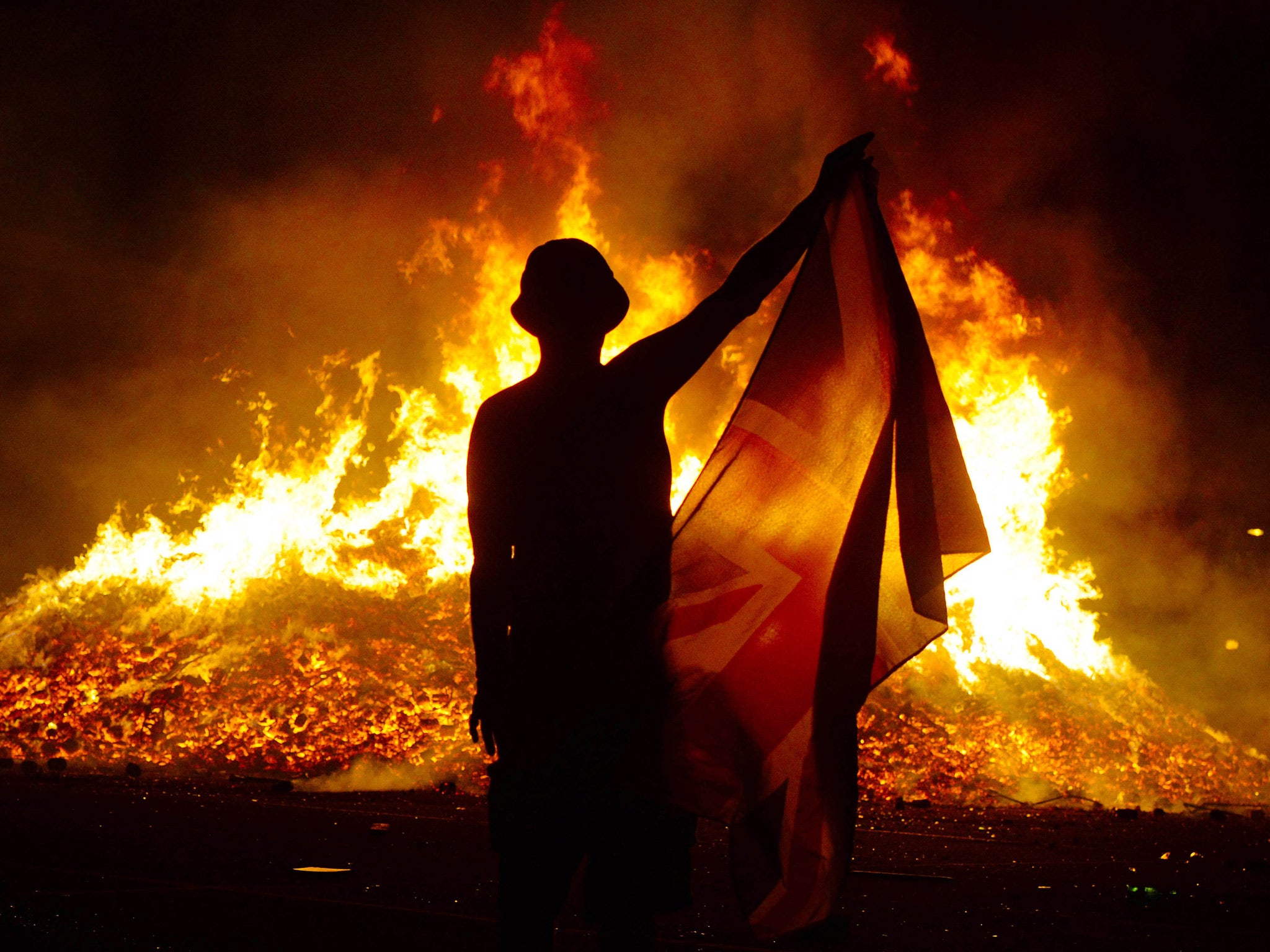 An unidentified man dances with a Union Jack flag and a protestant band flute in front of a Loyalist bonfire on Lanark WayJuly 12, 2014 in Belfast, Northern Ireland. The bonfires are lit on the stroke of midnight and mark the beginning of the annual 12th of July Orange parades in Northern Ireland. Source: Getty Images