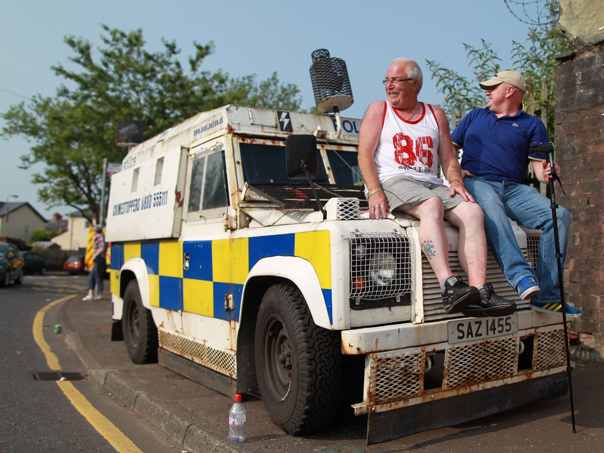 Two spectators sit on the bonnet of an armoured police vehicle as protestant Orangemen march through the Catholic Ardoyne district of north Belfast, Northern Ireland, on July 12, 2013. Source: Getty Images