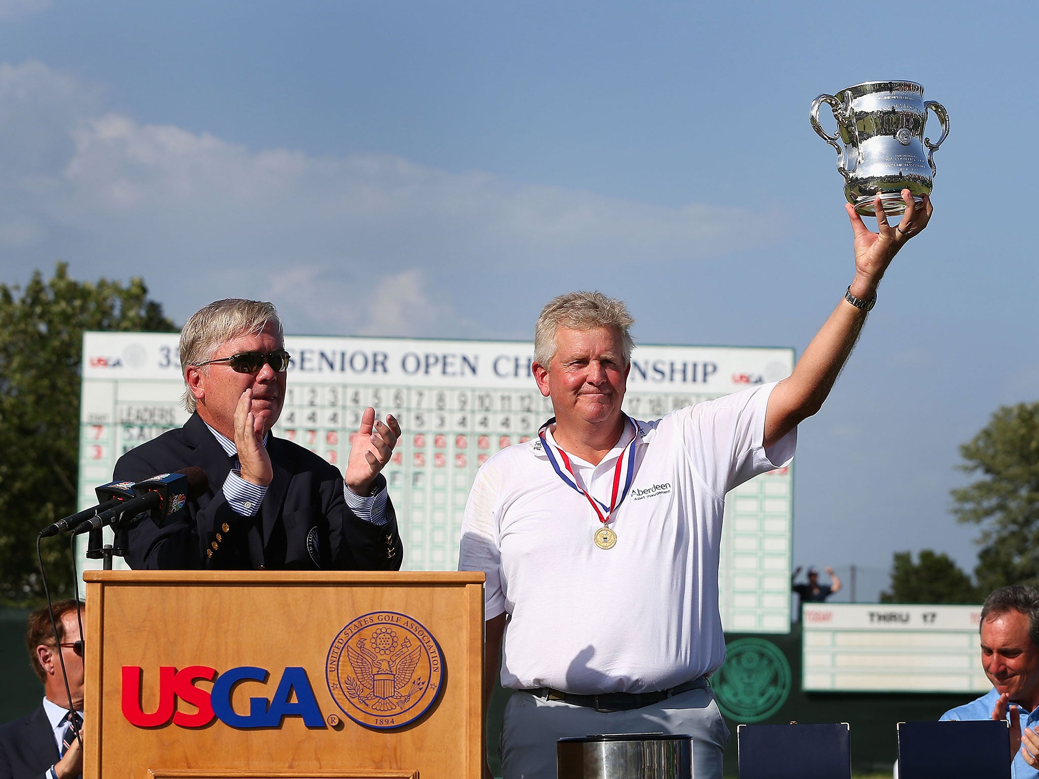 Colin Montgomerie (R) of Scotland lifts the winner's trophy, alongside USGA President Thomas J. O'Toole Jr., after winning the 2014 U.S. Senior Open Championship