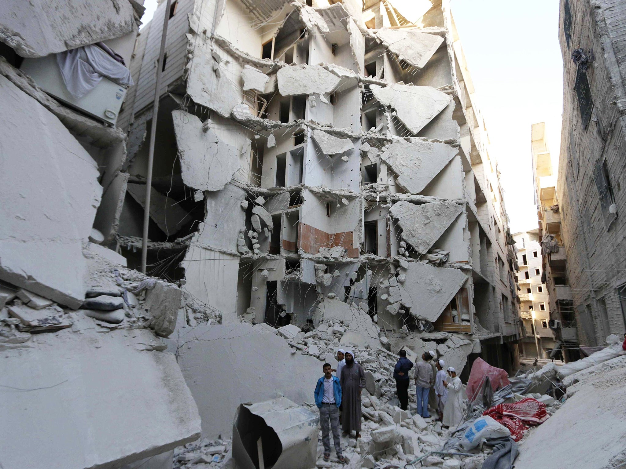 People stand on the rubble of collapsed buildings at a site hit by what activists said was a barrel bomb dropped by forces loyal to Assad, in the Al-Fardous neighbourhood of Aleppo