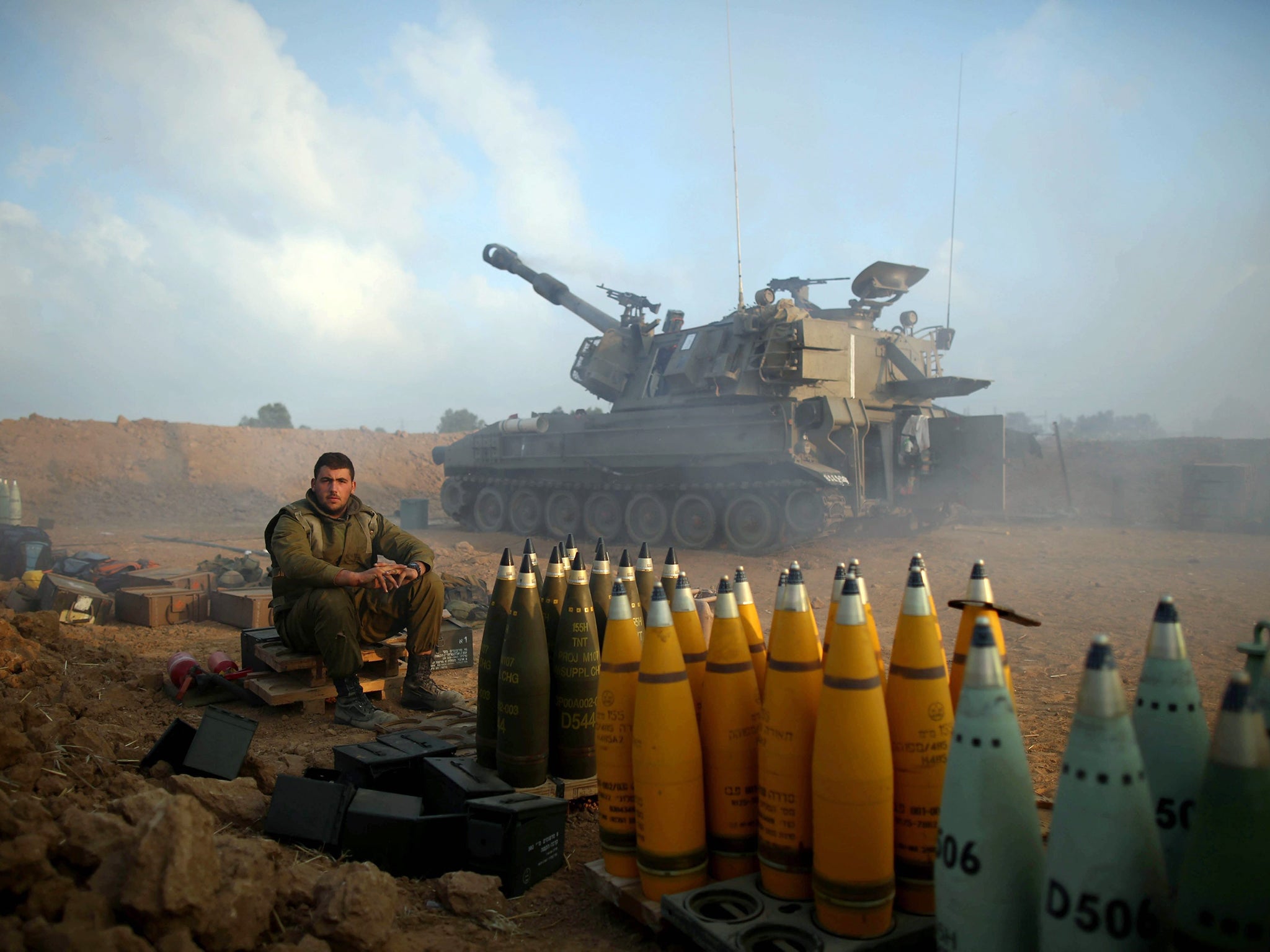 Israeli soldiers rest next to artillery shells from an artillery unit near the Israeli border with Gaza