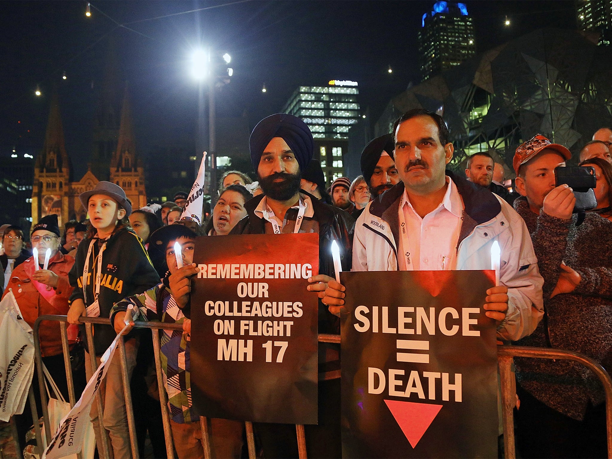 Members of the public hold candles to mourn the victims of HIV/AIDS and the victims of flight MH17 during a candlelight vigil at Federation Square in Melbourne, Australia