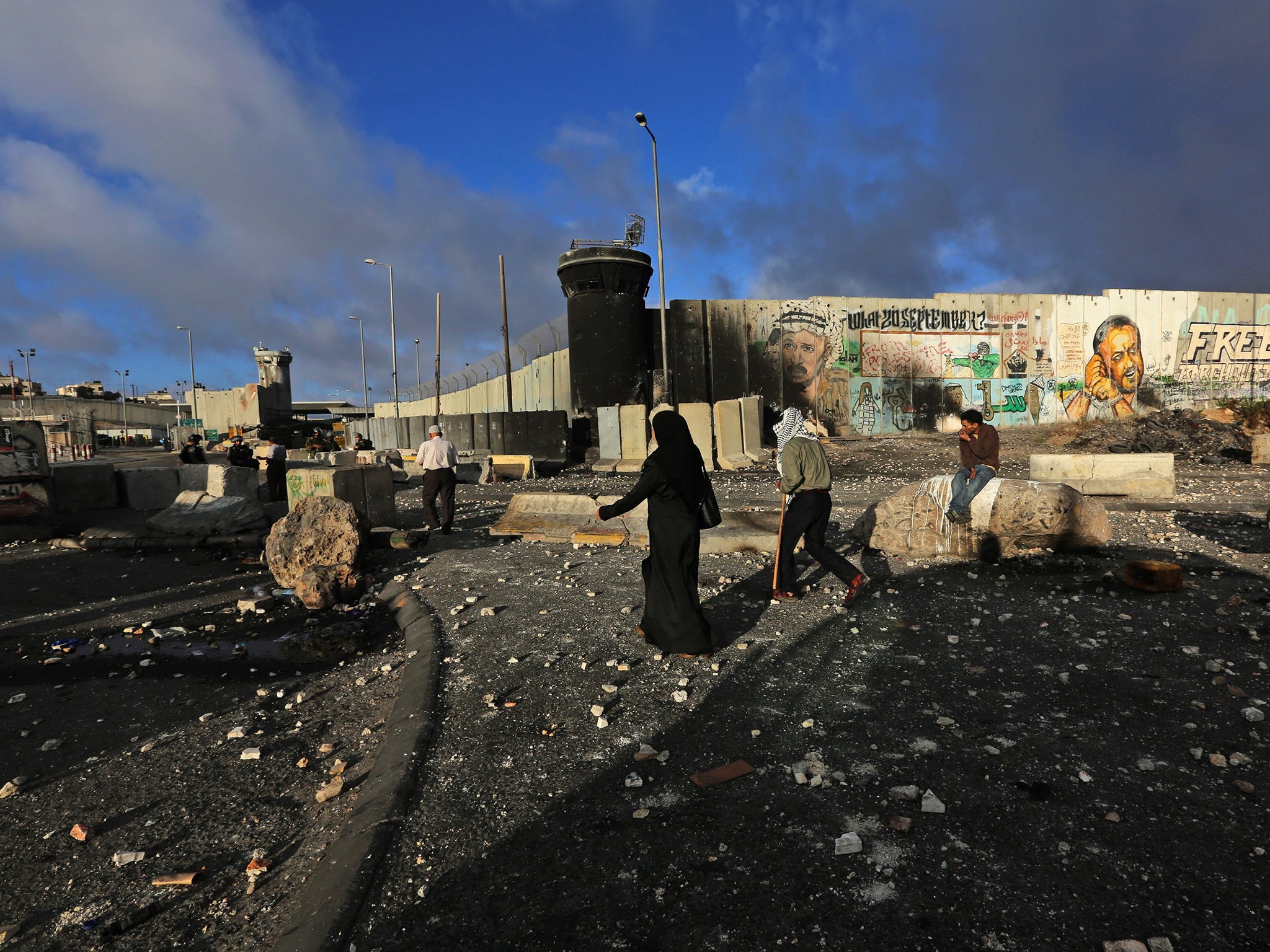 Palestinians walk on the street full of stones which were hurled in clashes between Palestinians and Israeli security forces fill the street in front of an Israeli watch tower of the Qalandia checkpoint near the West Bank city of Ramallah