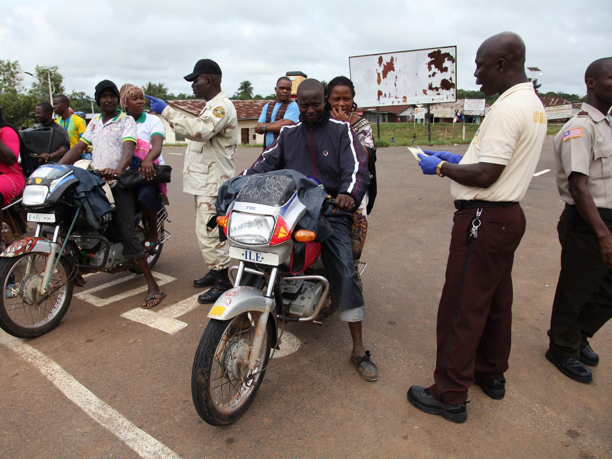 Liberia immigration officers wearing protective gloves inspect the travel documents at a border post with Sierra Leone, 30 July (EPA)