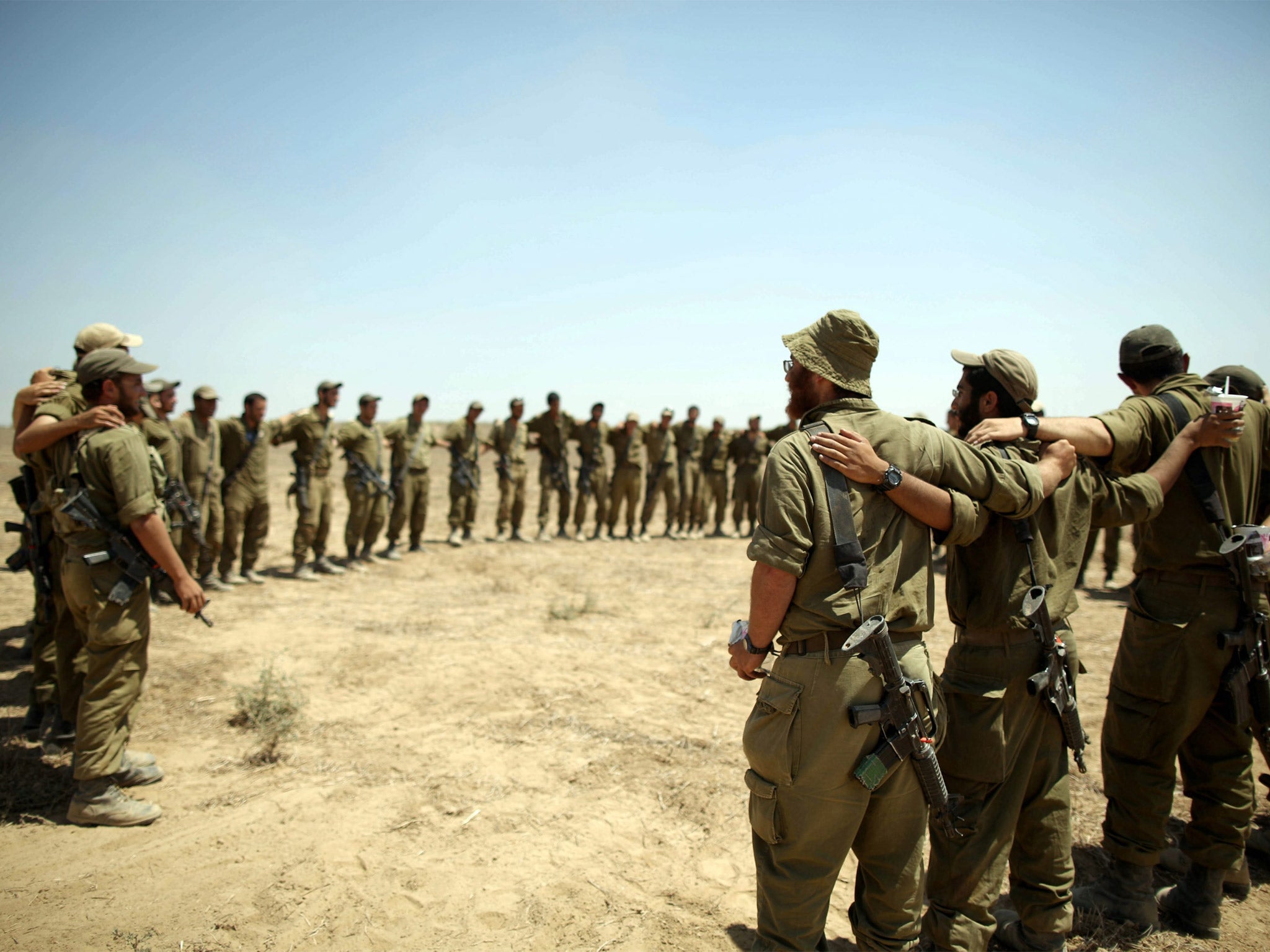 Israeli soldiers embrace each other as they sing at a staging area at an unspecified location near the Gaza border