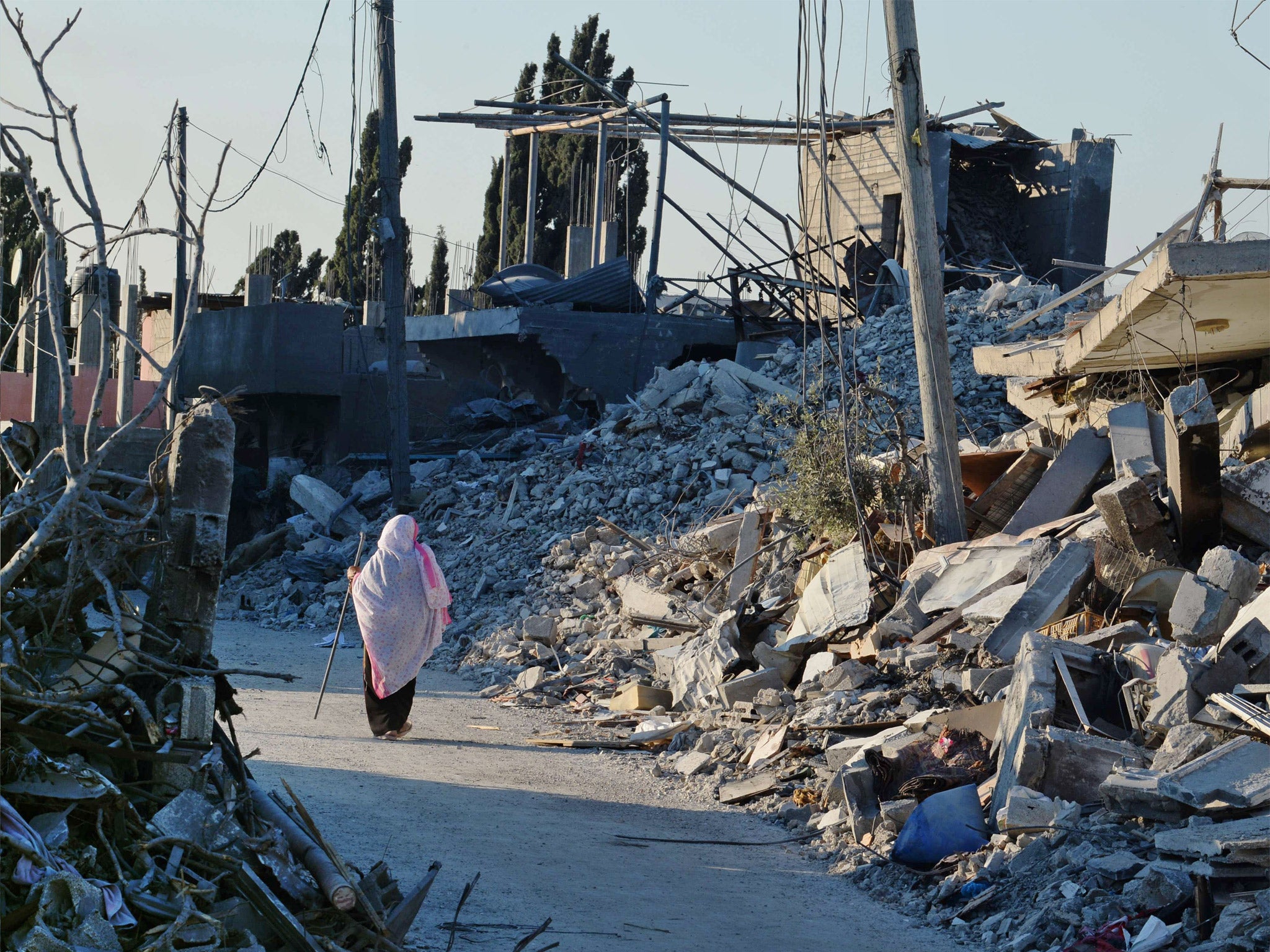 A Palestinian woman uses a piece of reebar she found amid the rubble, for support as she walks past destroyed homes in a street in Beit Hanun, northern Gaza