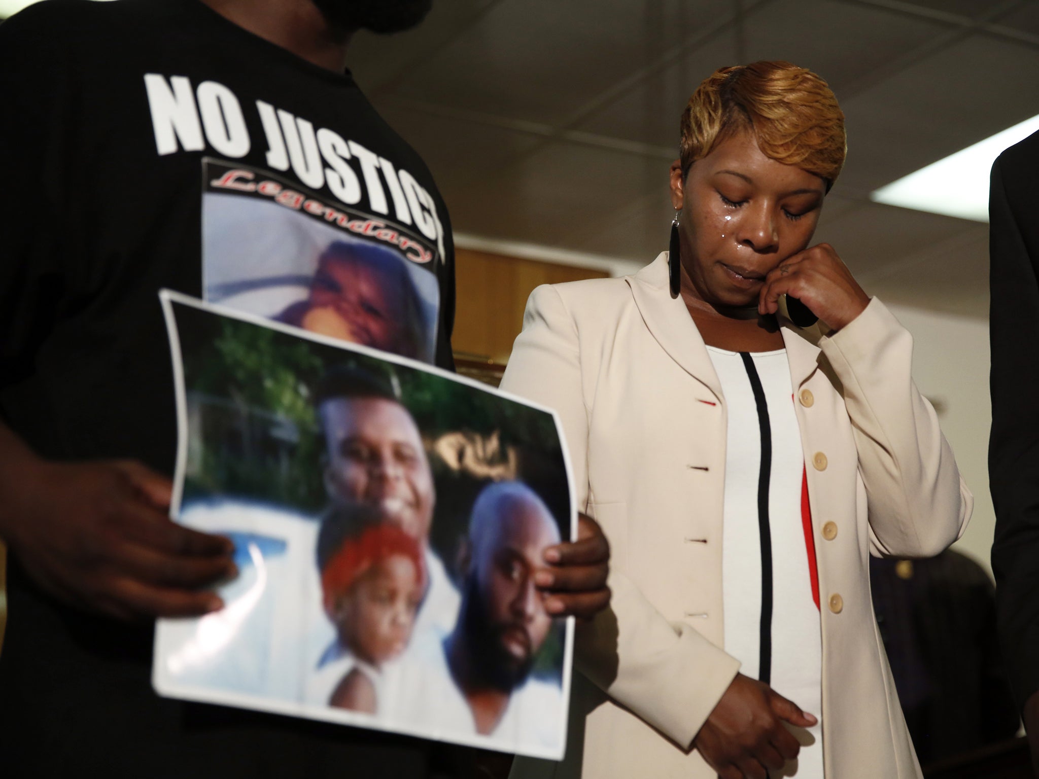 Lesley McSpadden, the mother of 18-year-old Michael Brown, wipes away tears as Brown's father, Michael Brown Sr., holds up a family picture of himself, his son, top left, and a young child during a news conference in Jennings