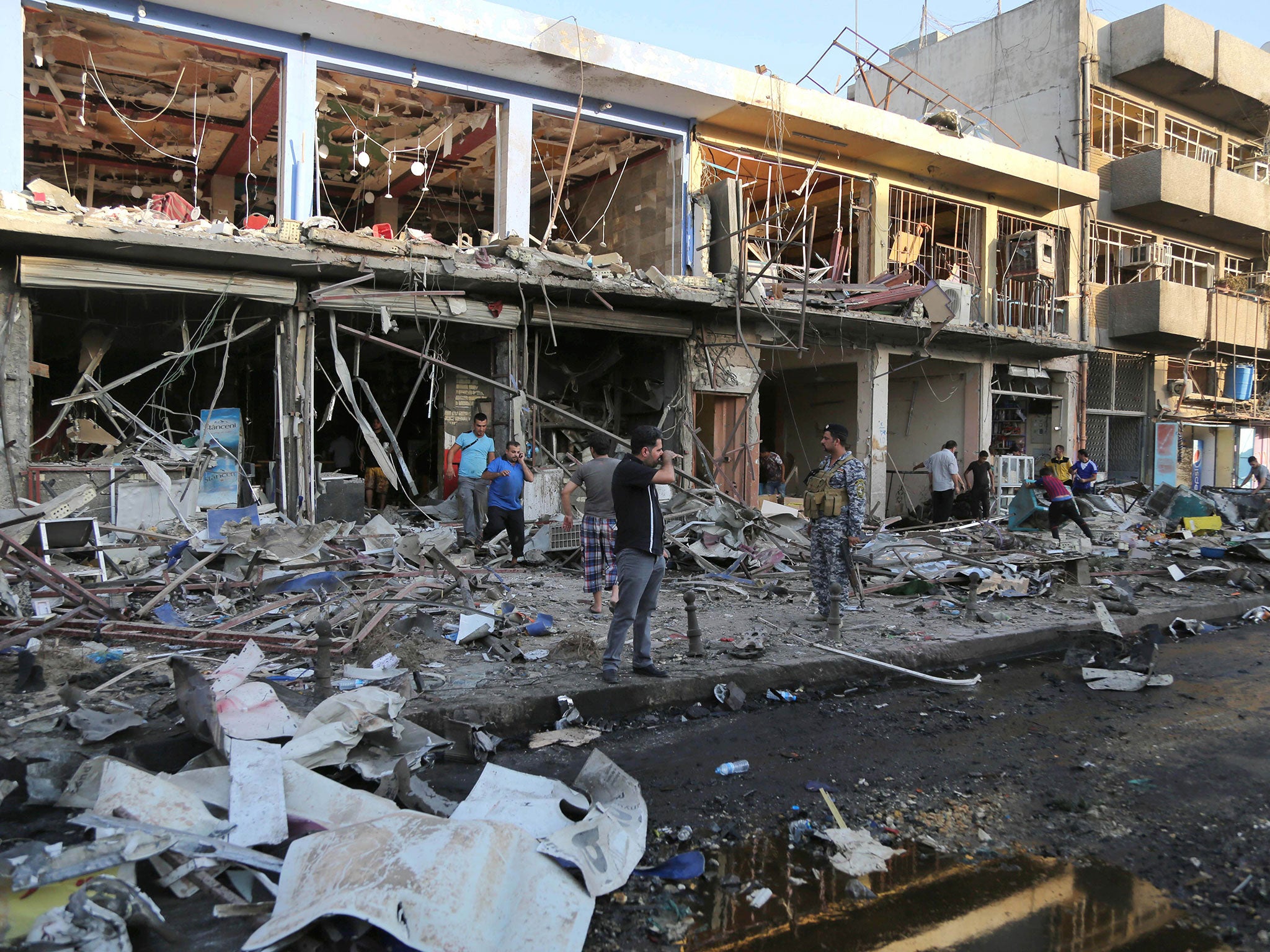 Iraqi policemen and civilians inspect the site of a car bomb attack near a restaurant in the southeastern district of New Baghdad