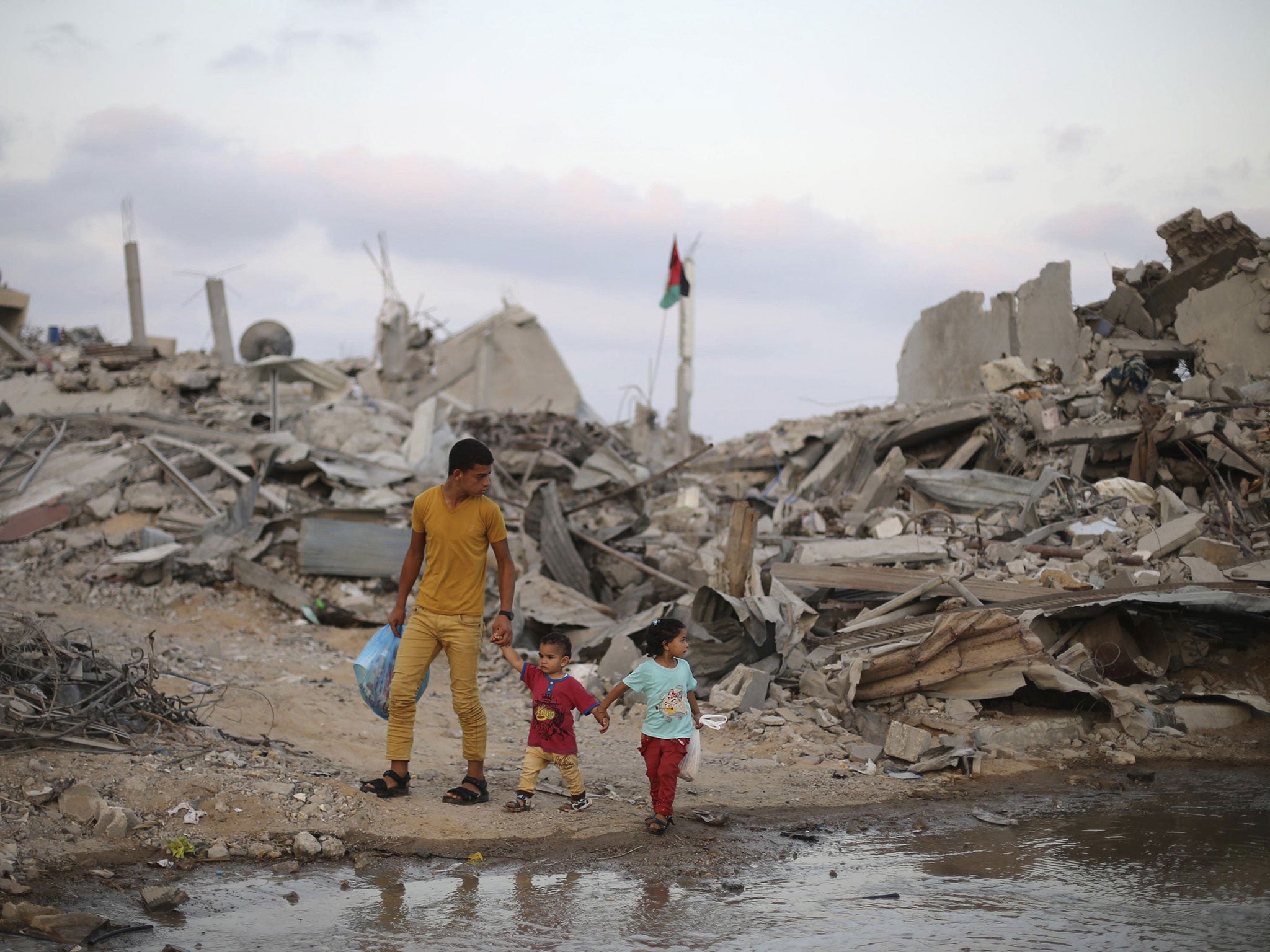 Palestinians walk next to the ruins of houses on the fifth day of ceasefire in Khan Younis in the southern Gaza Strip