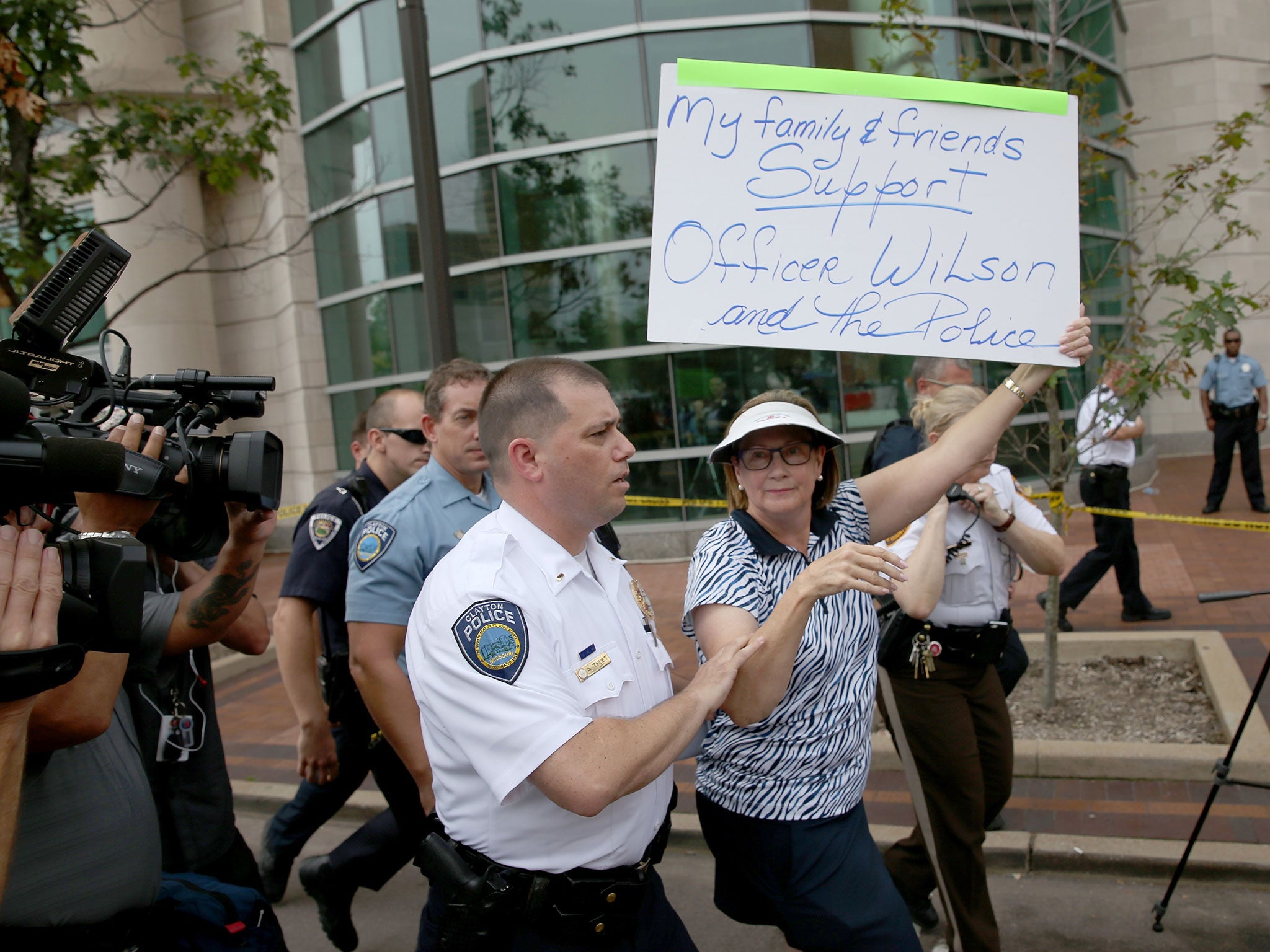 A police officer escorts Patty Canter who holds a sign reading, " My Family &amp; Friends Support Officer Wilson and the Police", away from protesters