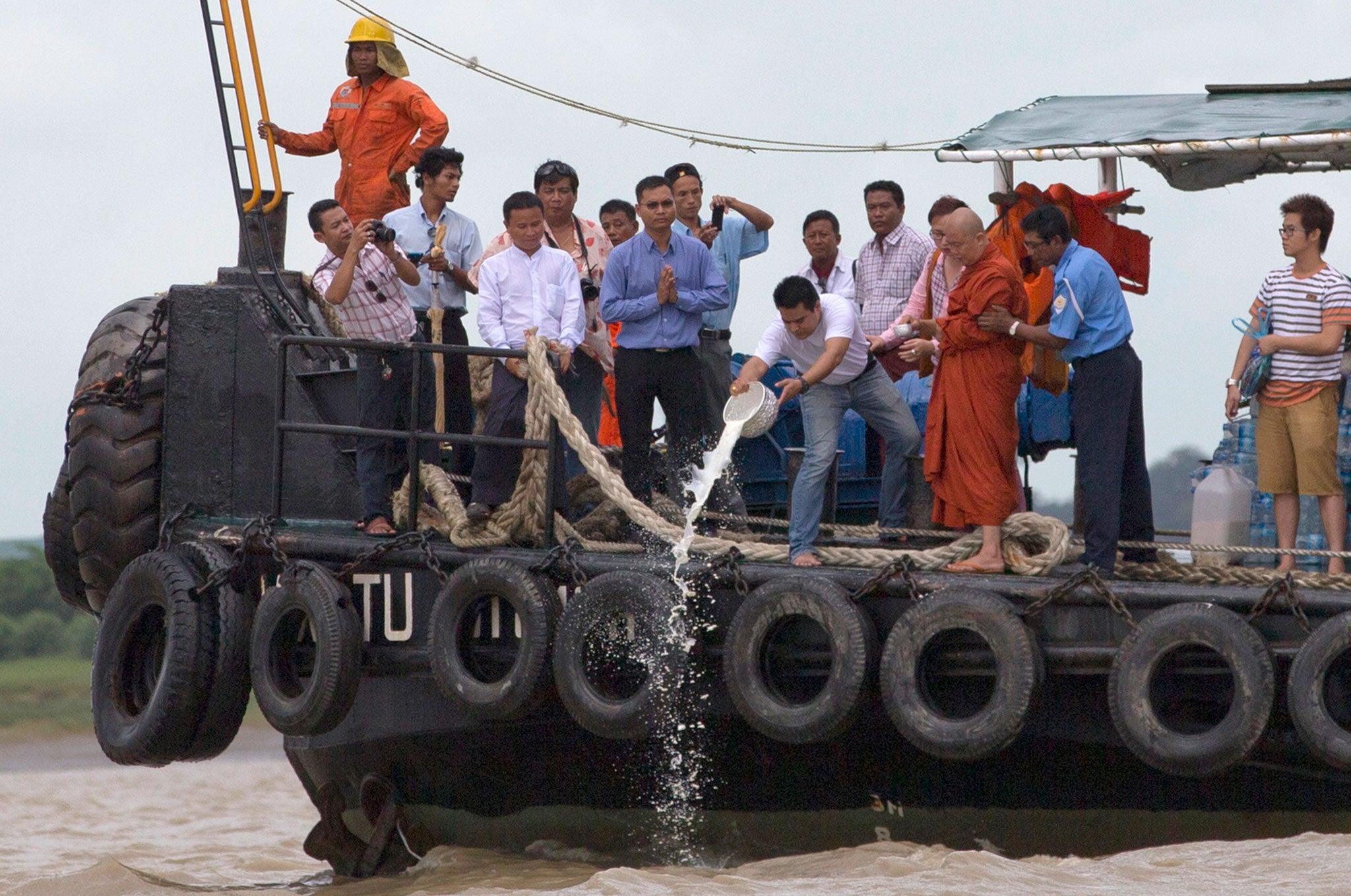 A man offers a basketful of milk from nats along with a monk and others before divers commence their search to recover an ancient bell in Yangon River in Yangon, Myanmar