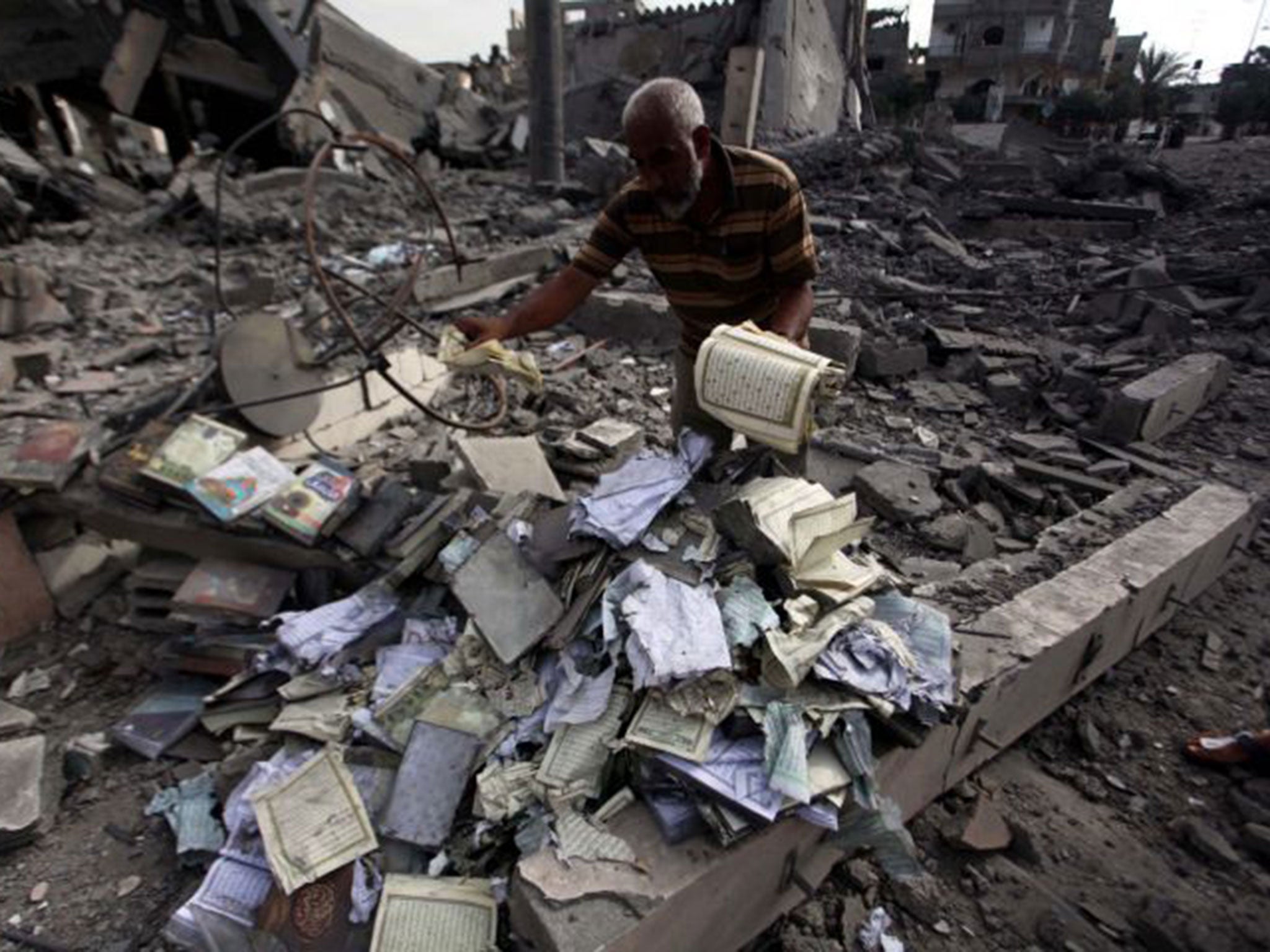 A Palestinian man collects copies of the Quran in the rubble of the Omar Ibn Abd al-Aziz mosque destroyed in an Israeli air strike in Beit Hanoun