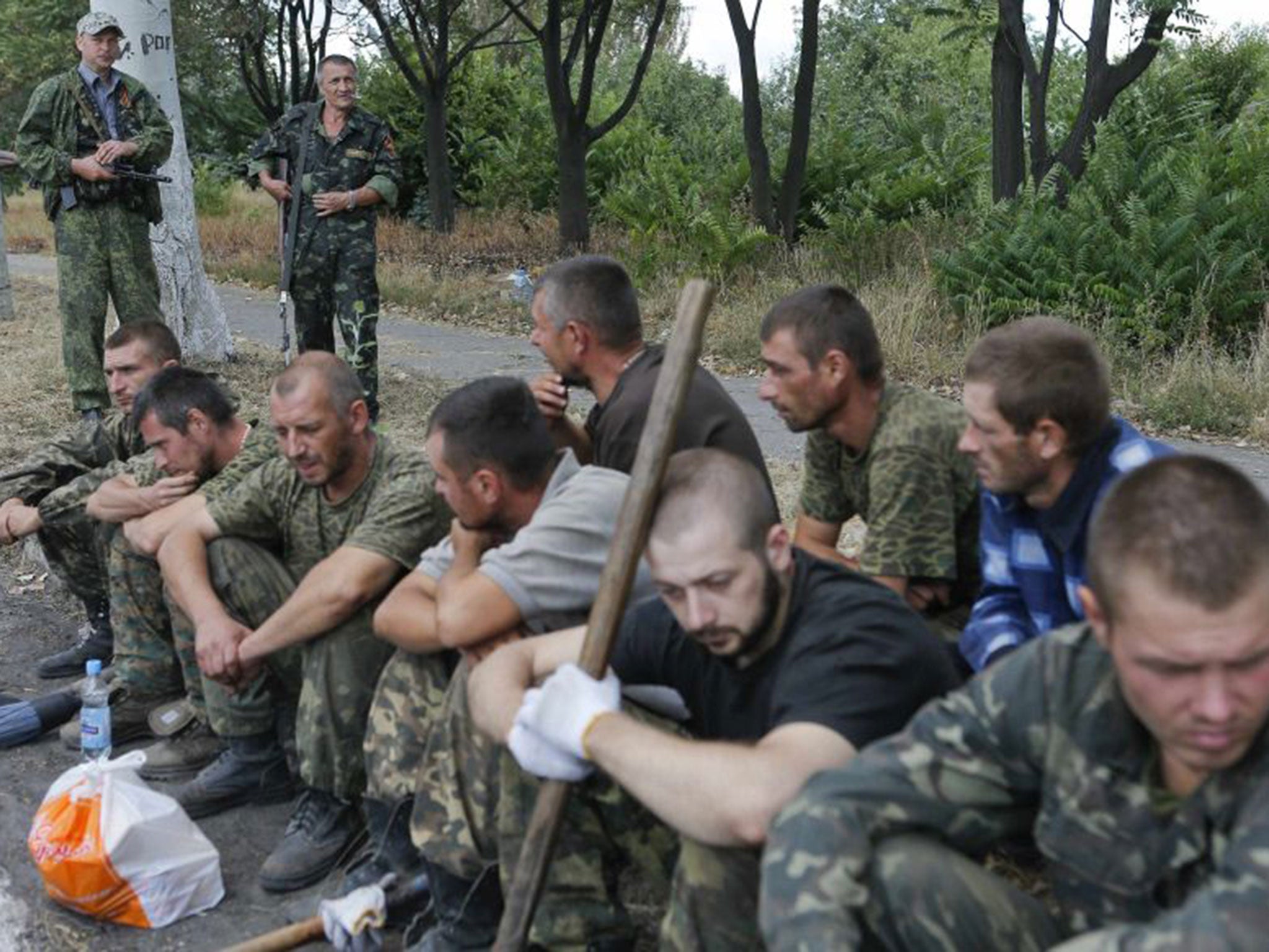 Ukrainian servicemen captured by pro-Russian separatists sit on the ground as they are assigned to clean a street in Snizhne in the Donetsk region
