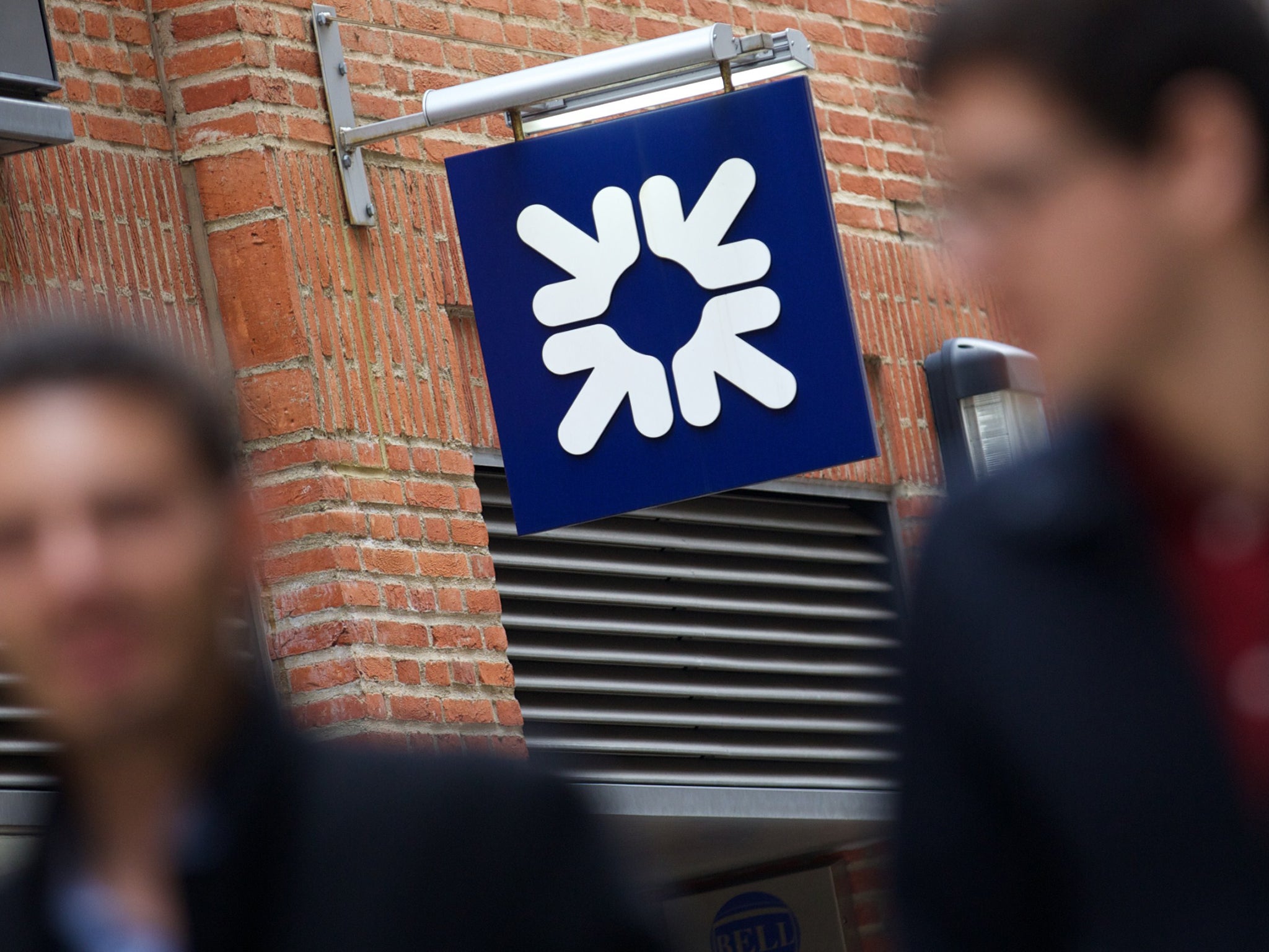 People walk past a Royal Bank of Scotland sign.