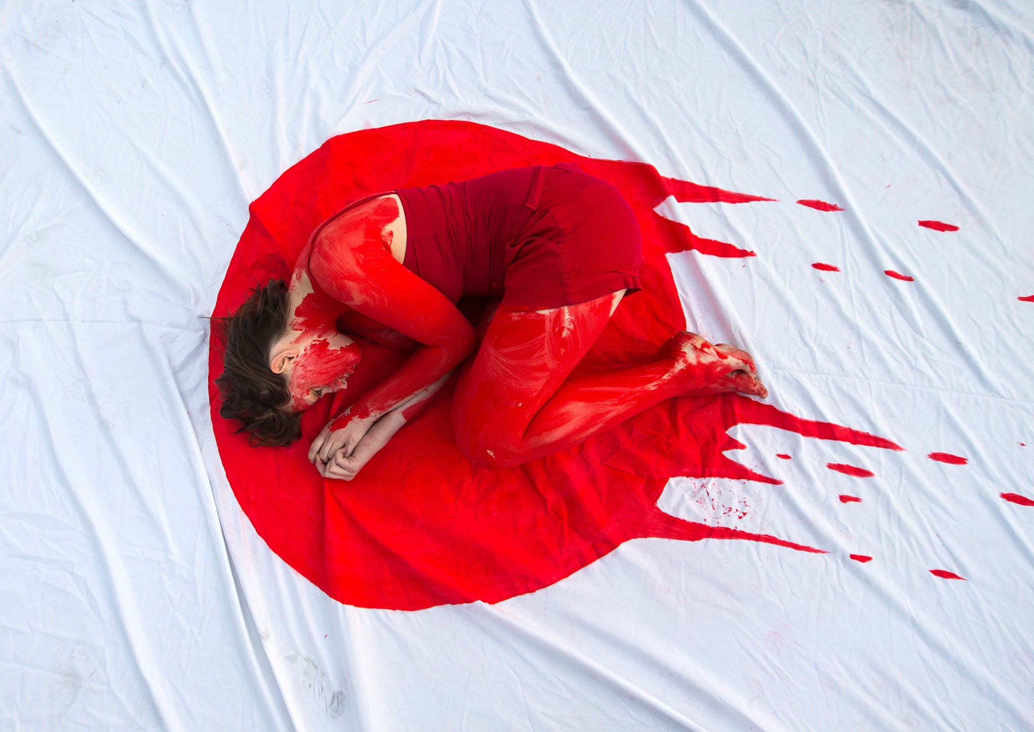 A member of the 'Taiji Dolphin Action Group' curls up on a sheet depicting the Japanese flag, during a protest against the killing of dolphins