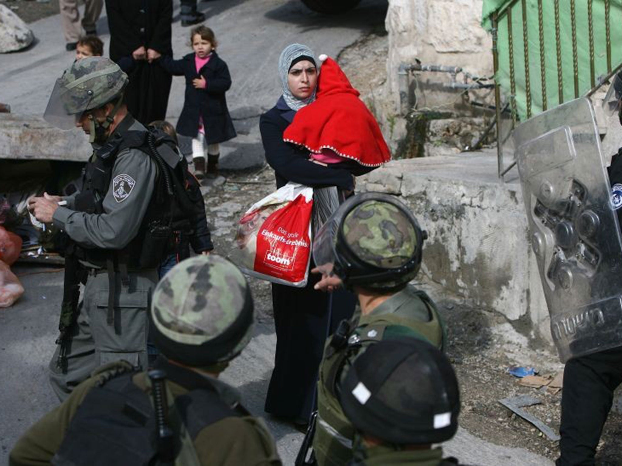 A Palestinian woman holds her baby while an Israeli army bulldozer demolishes a house in Jerusalem