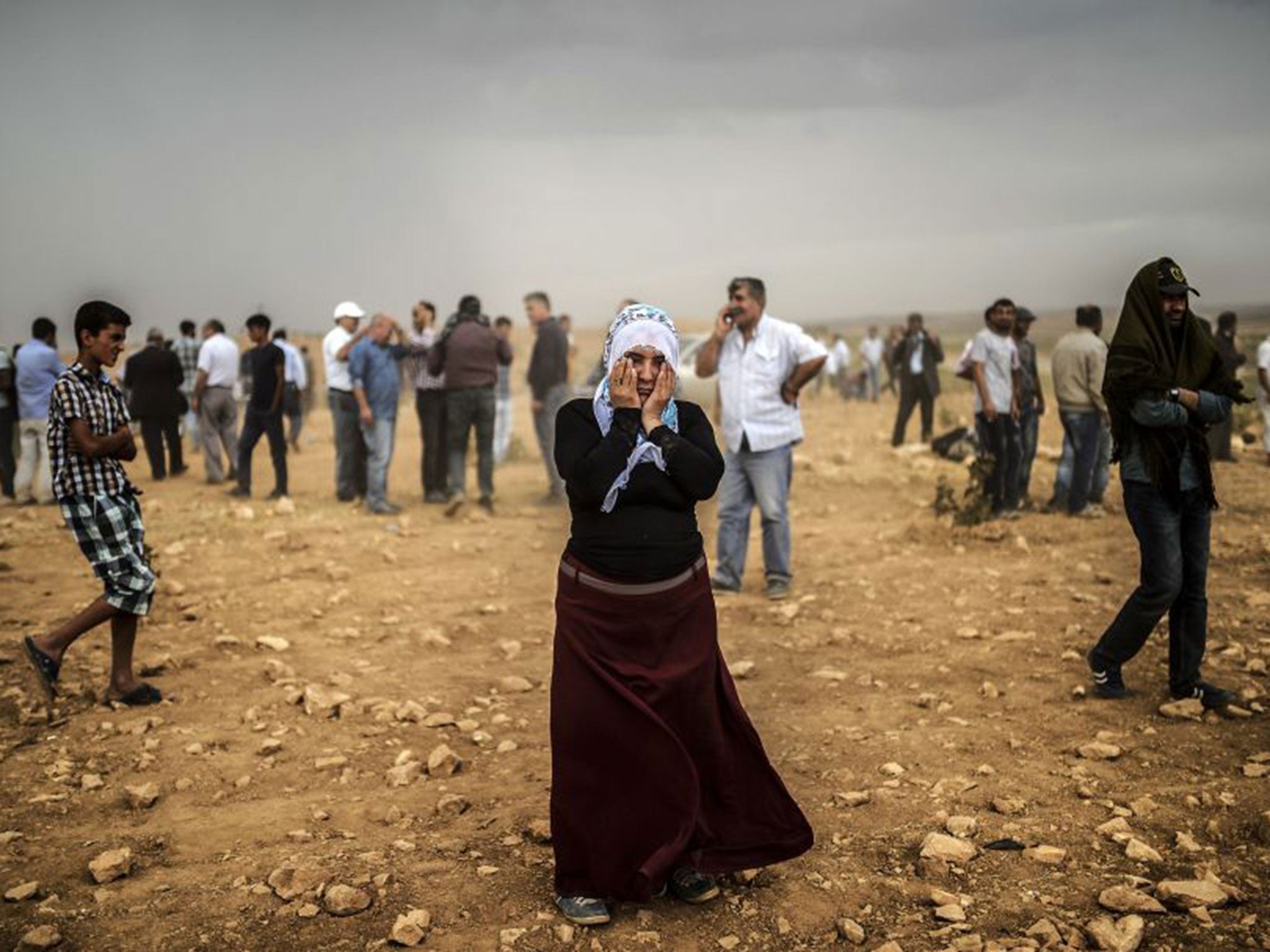 A Syrian Kurdish woman wipes her eyes during a dust storm on a hill from where people watch the battle with Isis