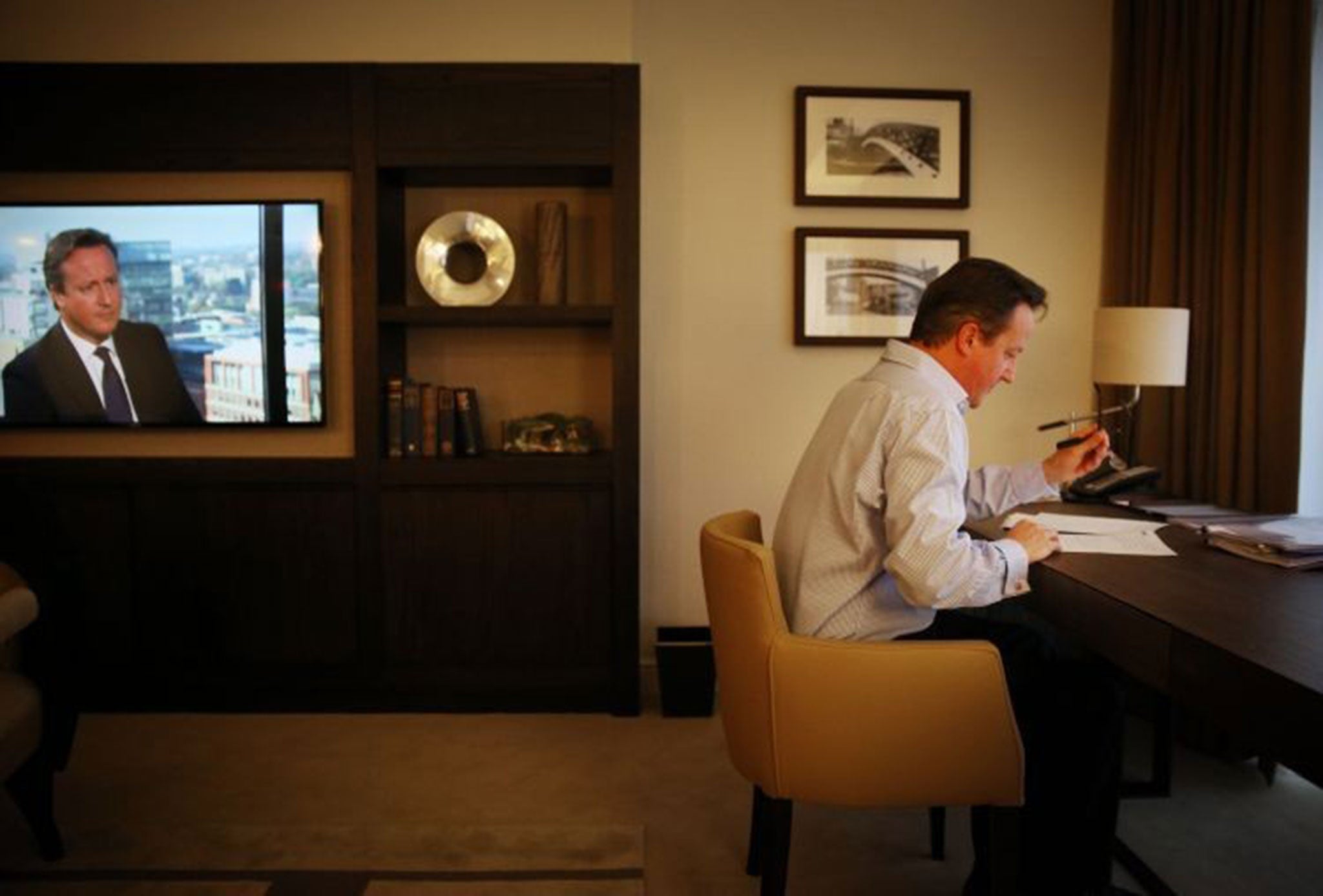 David Cameron prepares his keynote speech in his hotel room at the Conservative party conference as his image appears on a TV news broadcast