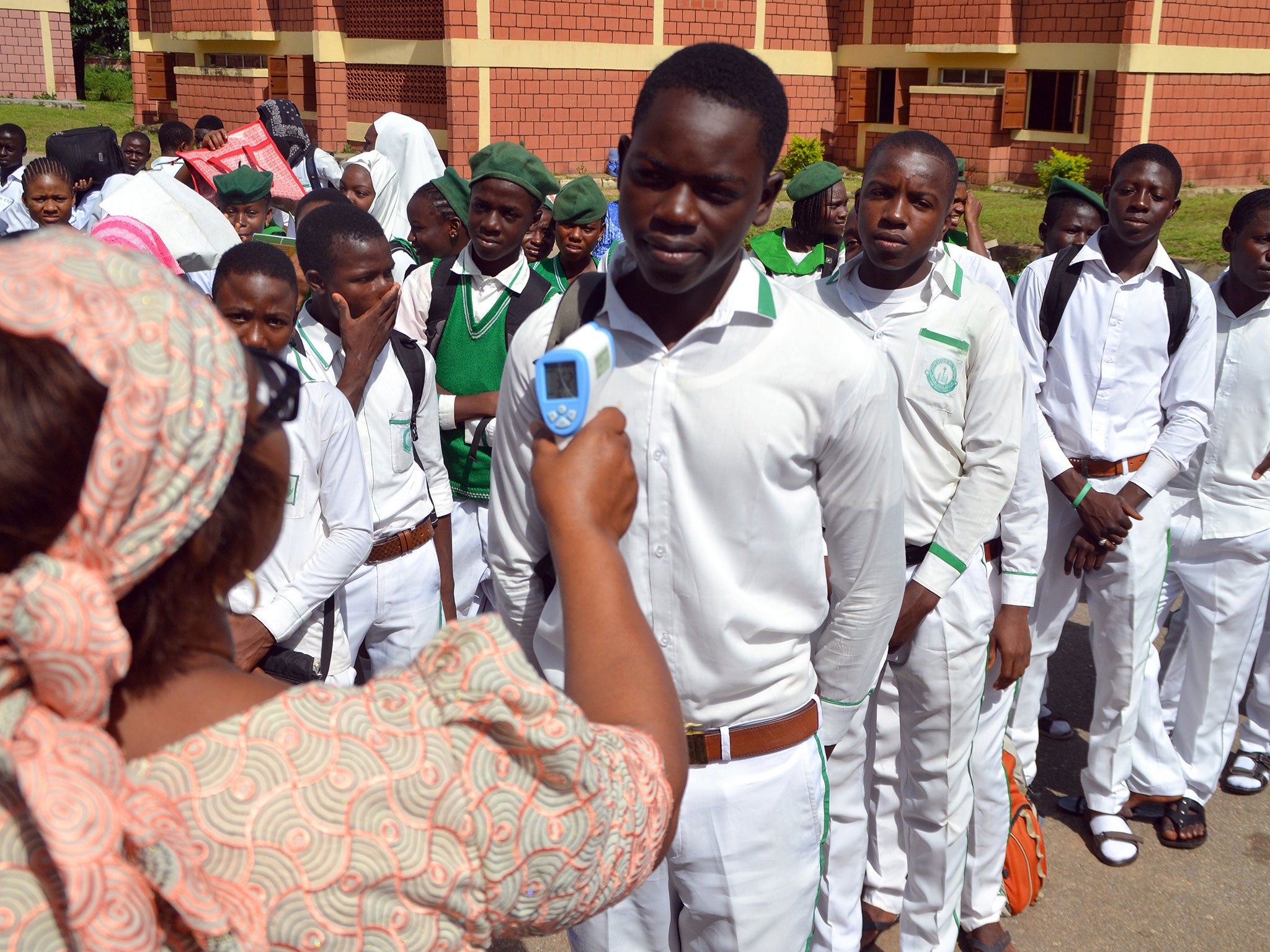 A secondary school principal checks a student's temperature for ebola symptoms during an assembly in Abuja