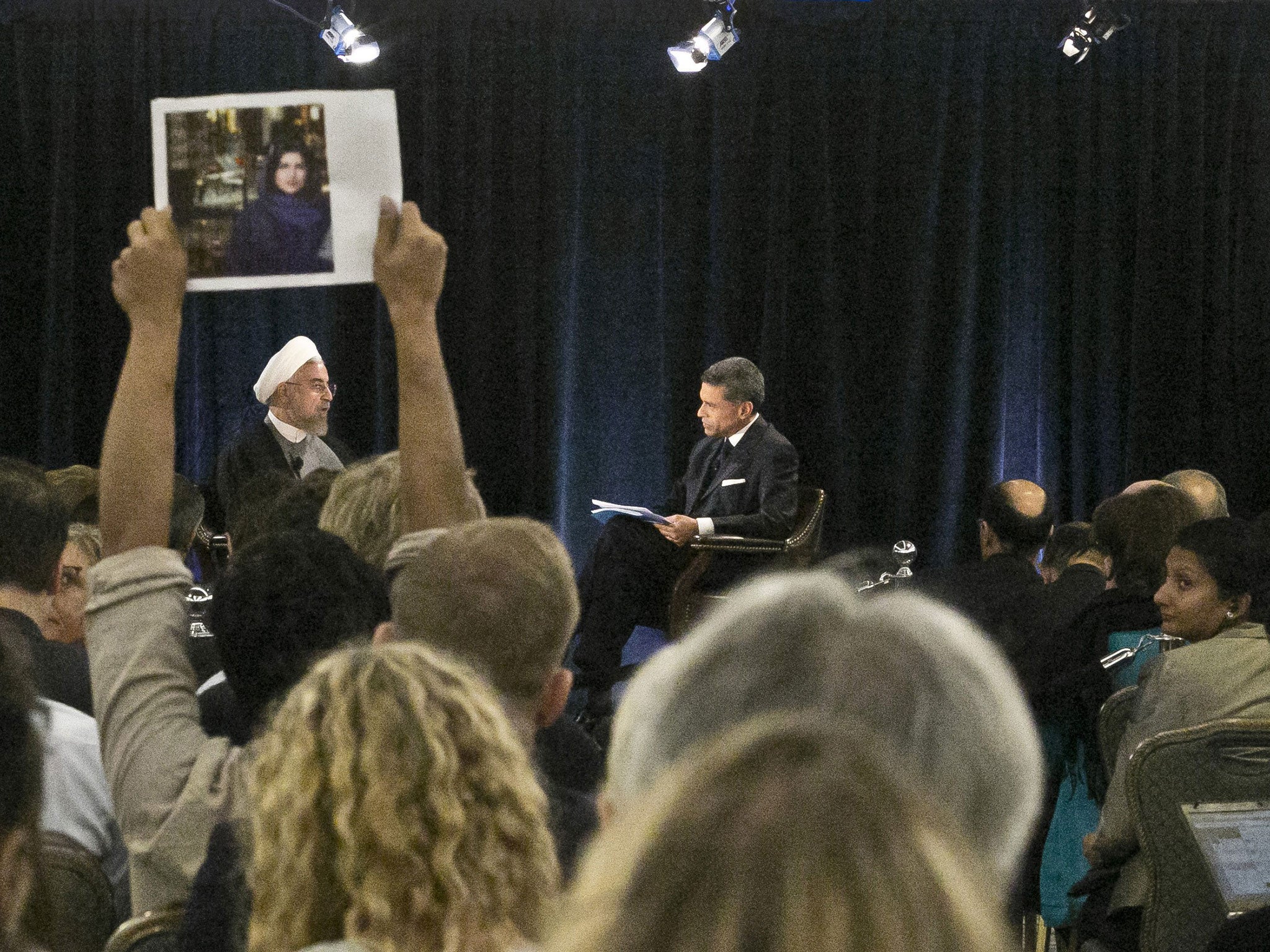 A protester holds up a picture of Ghoncheh Ghavami as Iran's President Dr. Hassan Rouhani, left, speaks with moderator Fareed Zakaria at New America, a public policy institute and think tank in New York on Wednesday, Sept. 24, 2014