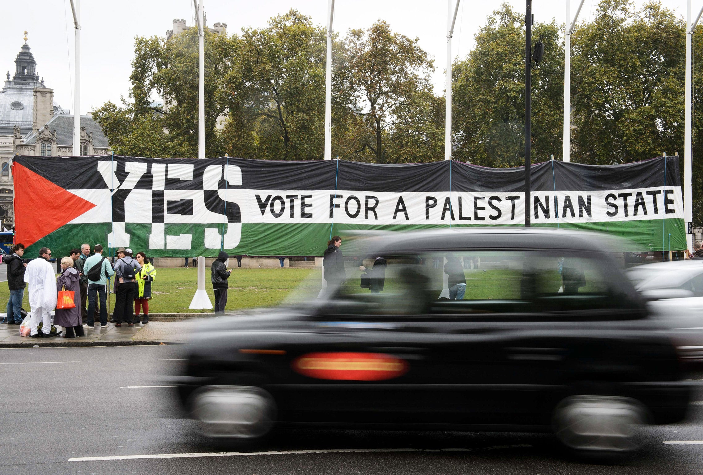 A taxi drives by as Pro-Palestinian supporters position a giant banner calling for a recognised Palestinian State, in Parliament Square, London (Getty)