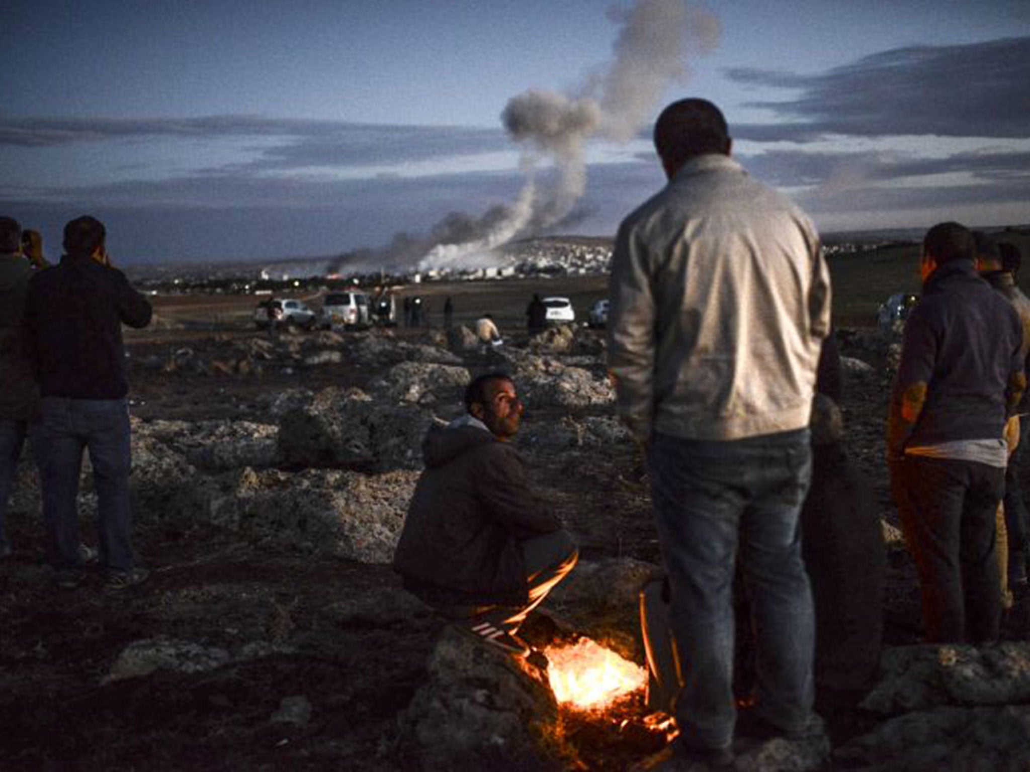 The US and Turkey have stepped up support for Kurdish fighters defending Kobani against Isis but it is still feared the town may fall; above, observers watch the fighting from a nearby village