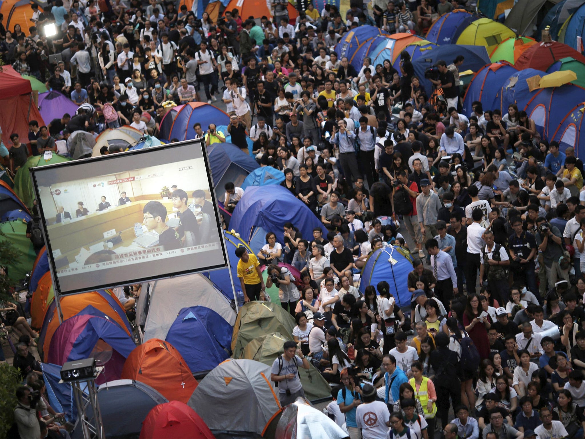 Protestors watch talks between student leaders and city officials on a video screen