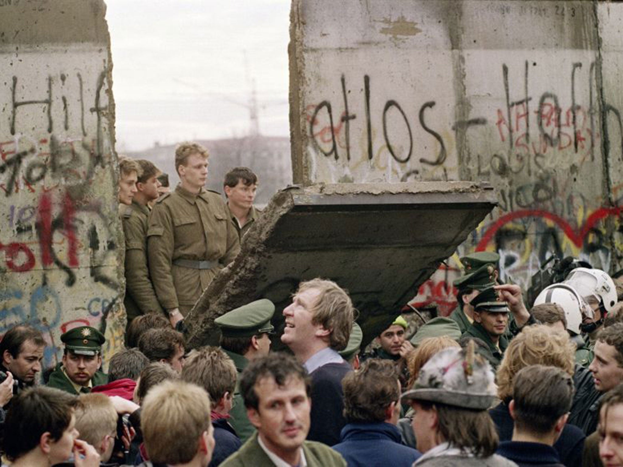 Police from both sides stand idly by as the Berlin Wall is breached for the first time between East and West, in November 1989 (Getty)