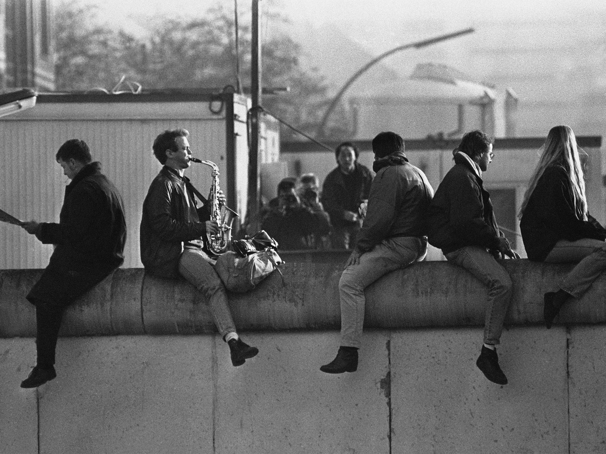 An East Berliner sits astride the wall playing his Saxaphone days after the toppling of the GDR