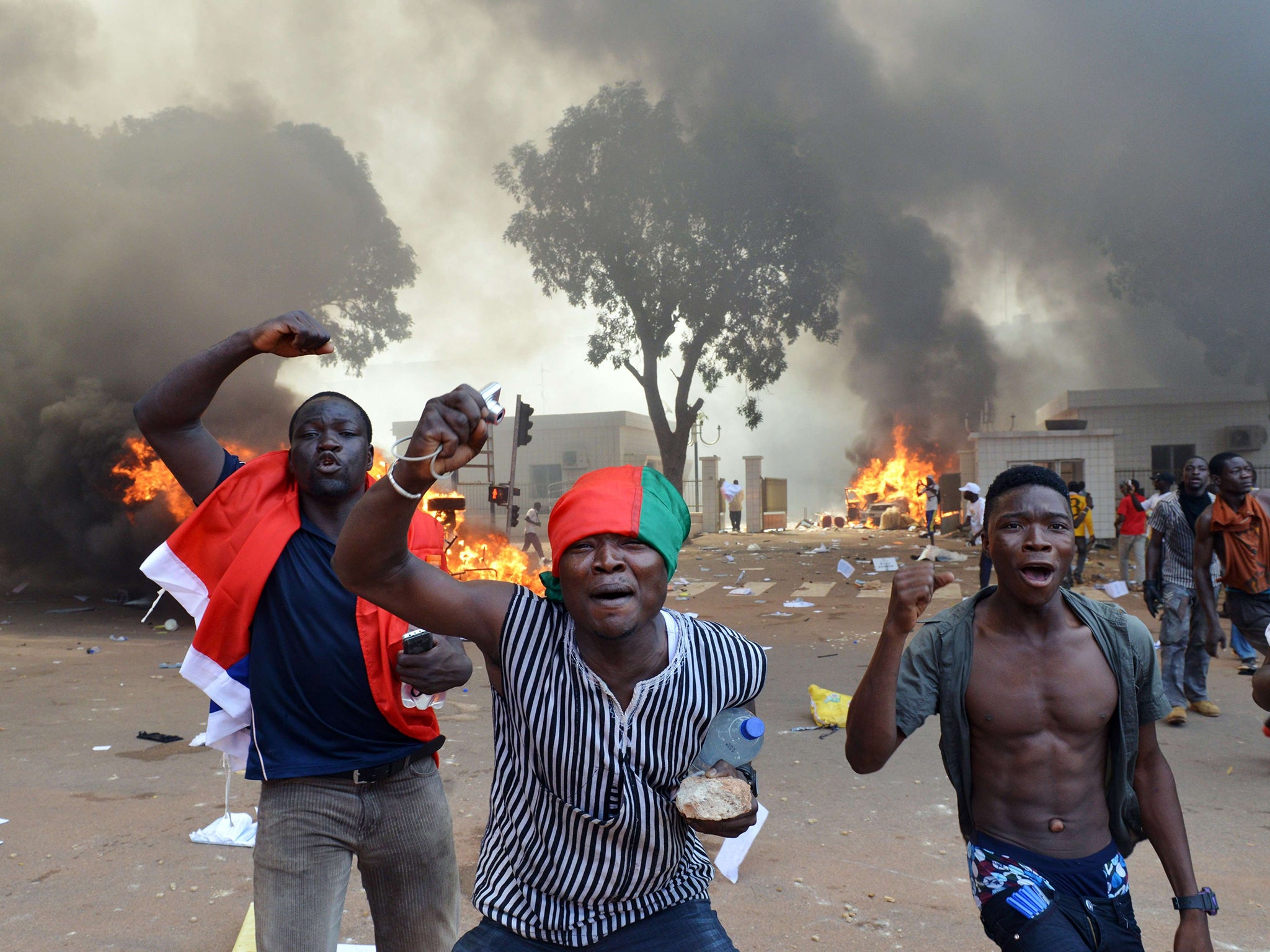 Men shout slogans in front of burning cars, near the Burkina Faso's Parliament