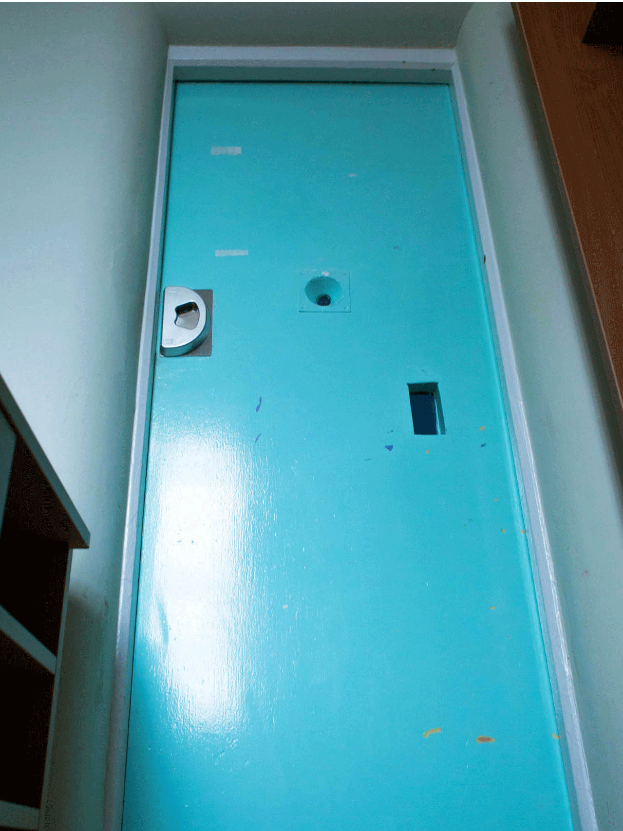 A heavy-duty door of a bedroom with a peep-hole for staff to observe a patient from