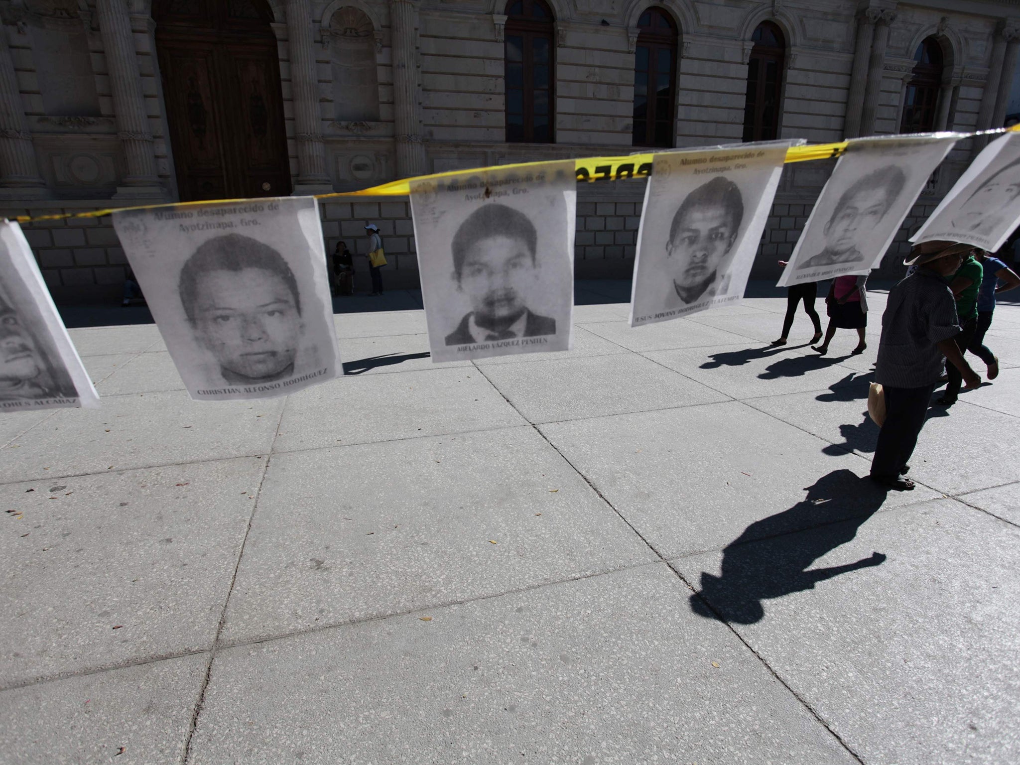 People walk near photographs of the missing student teachers from the Ayotzinapa Teacher Training College Raul Isidro Burgos, in Chilpancingo