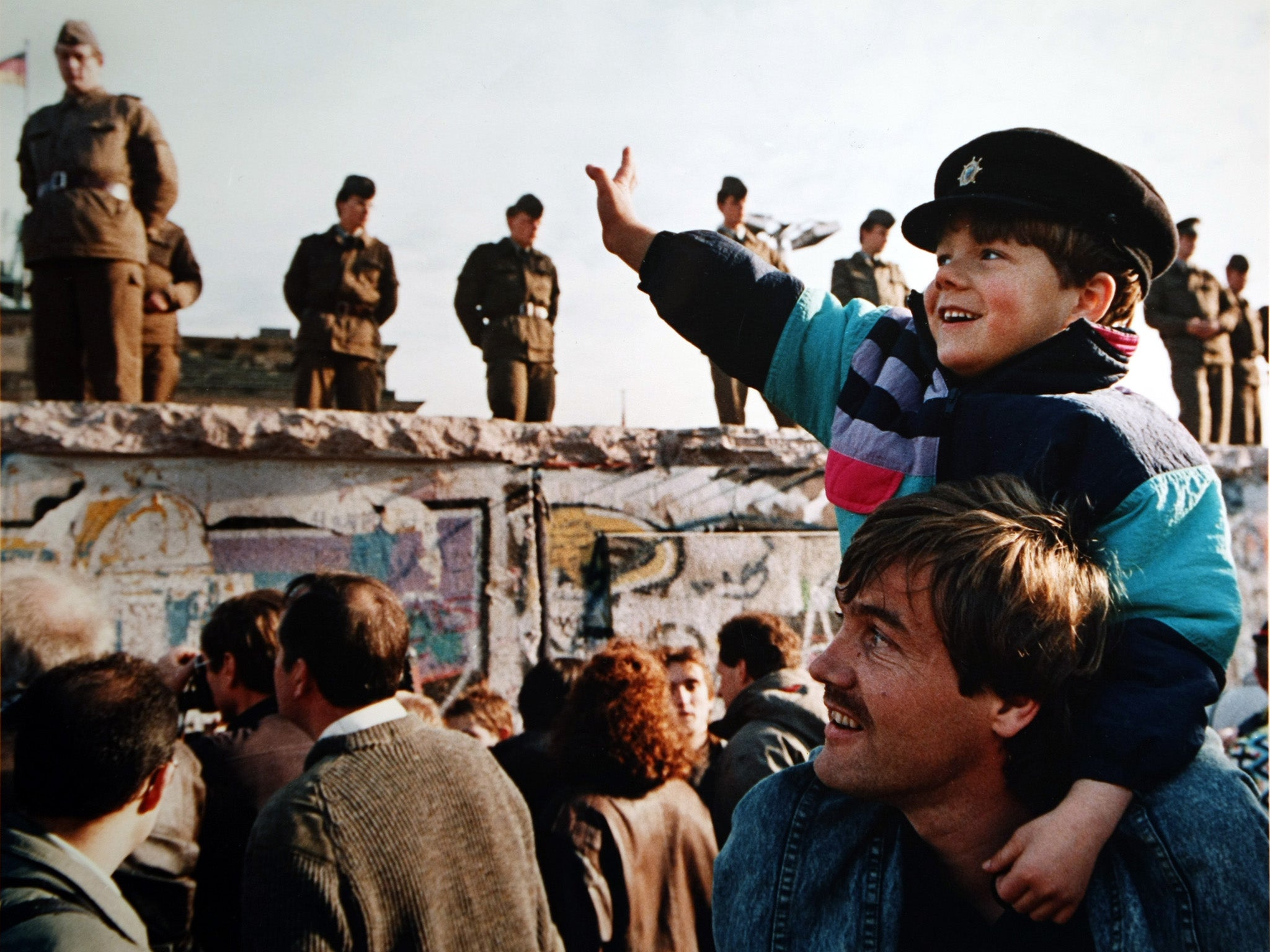 A boy waves to soldiers on the Berlin Wall in front of the Brandenburg Gate. (Photo by John Tlumacki/The Boston Globe via Getty Images)