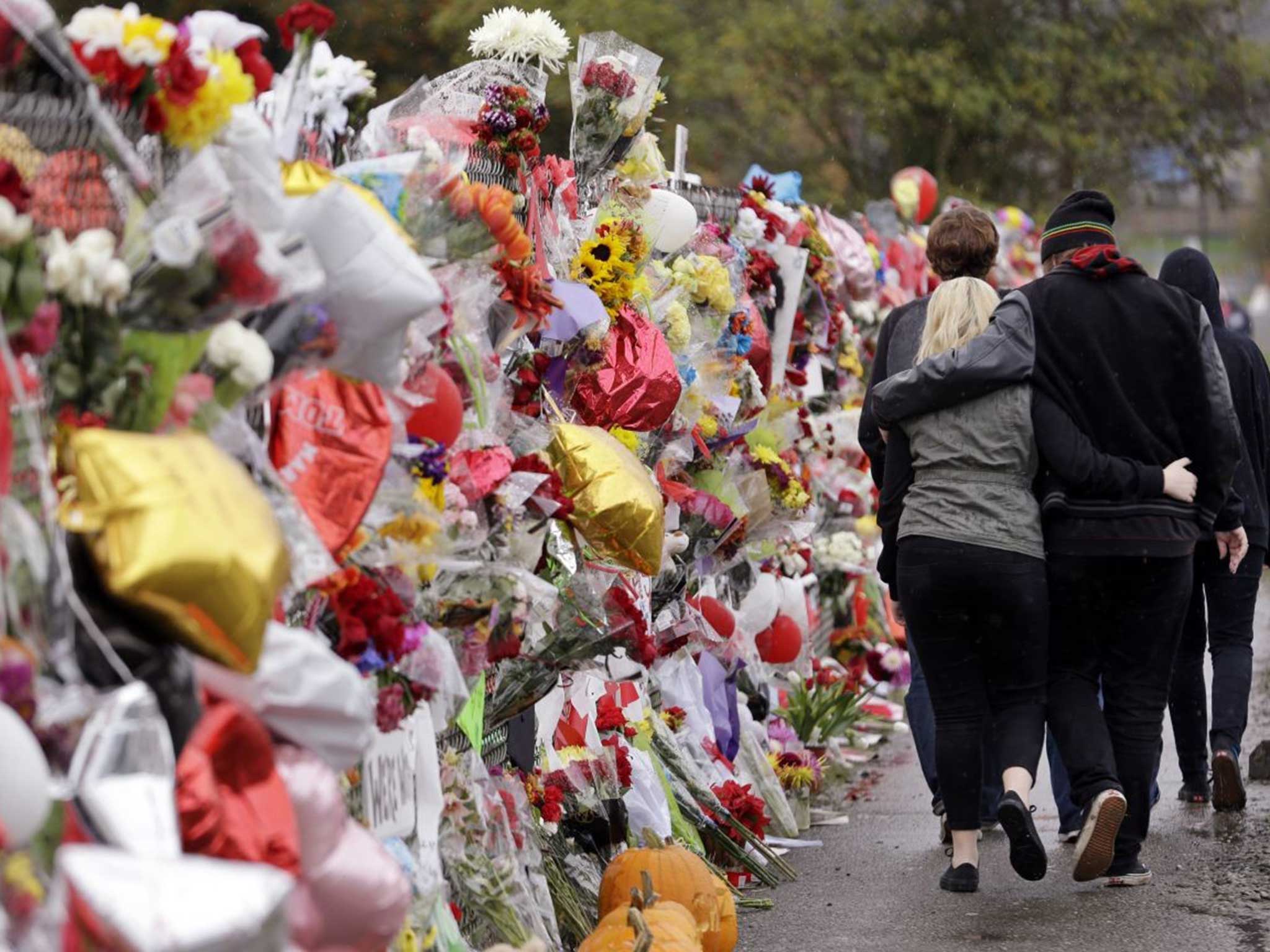 Mourners walk along one of the fences surrounding the school, now covered in messages and tributes to the young students killed