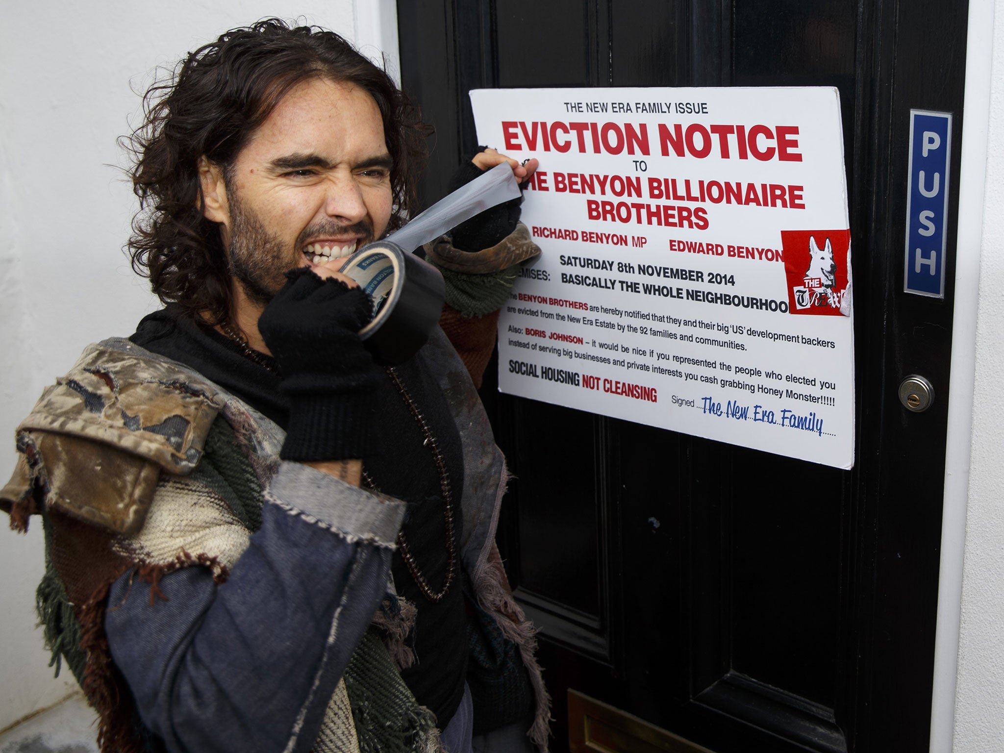 Russell Brand puts a fake eviction notice on The Benyon Estate office as he joins a group of east London residents who protest against rising housing prices