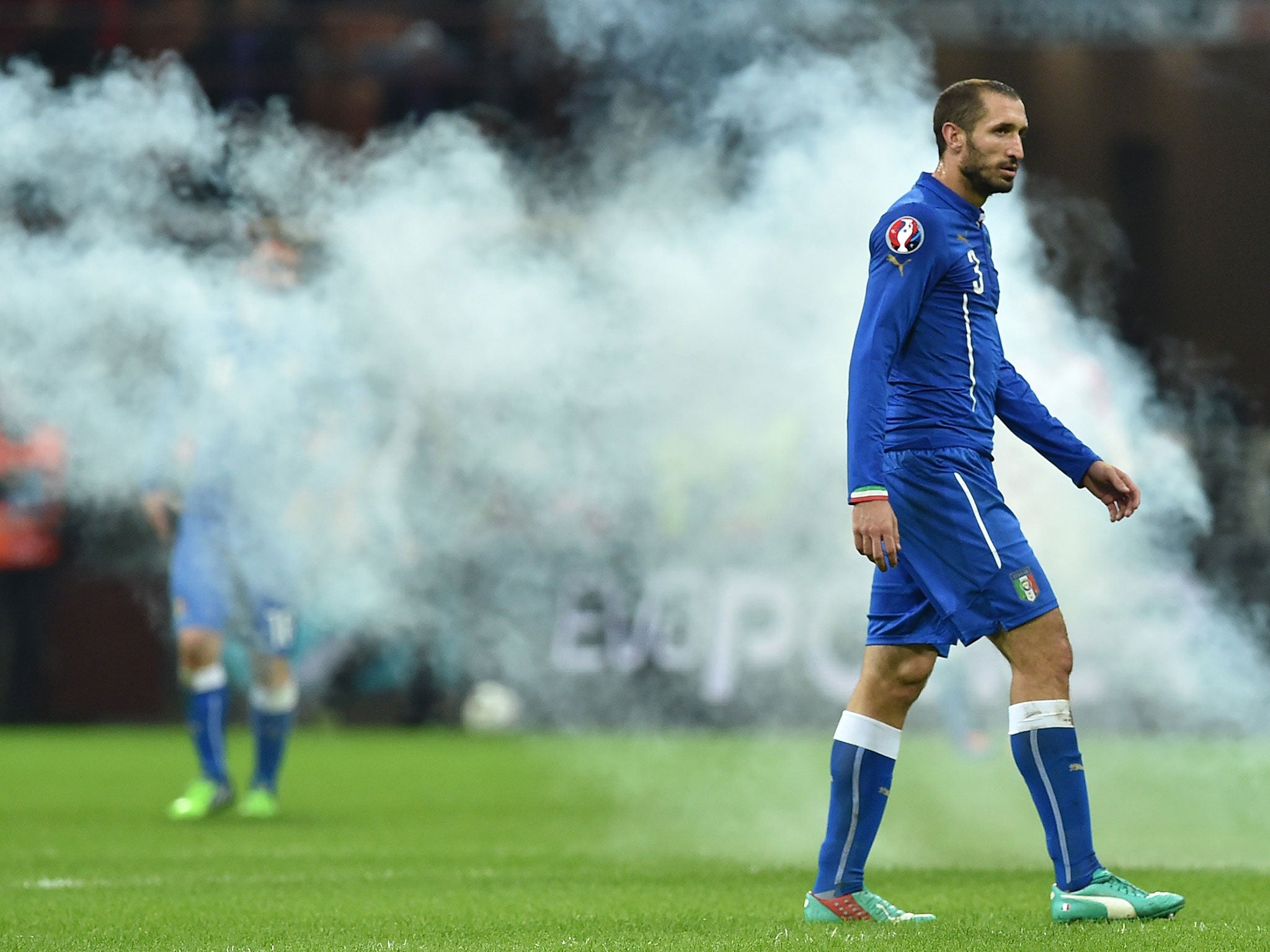 Giorgio Chiellini walks off the pitch as a flare burns in the background