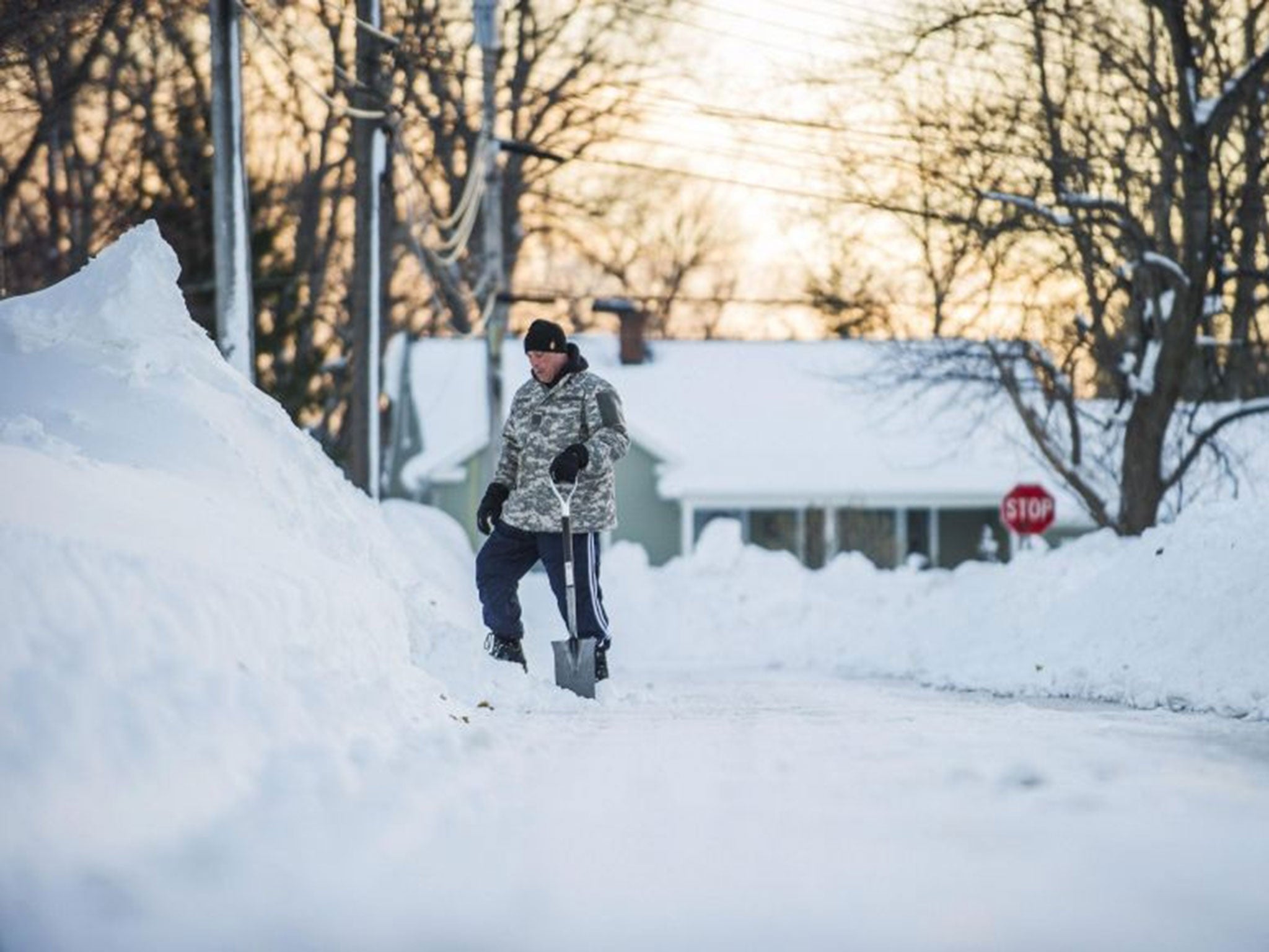 A man with a shovel looks at a tall snowbank in Buffalo, New York,