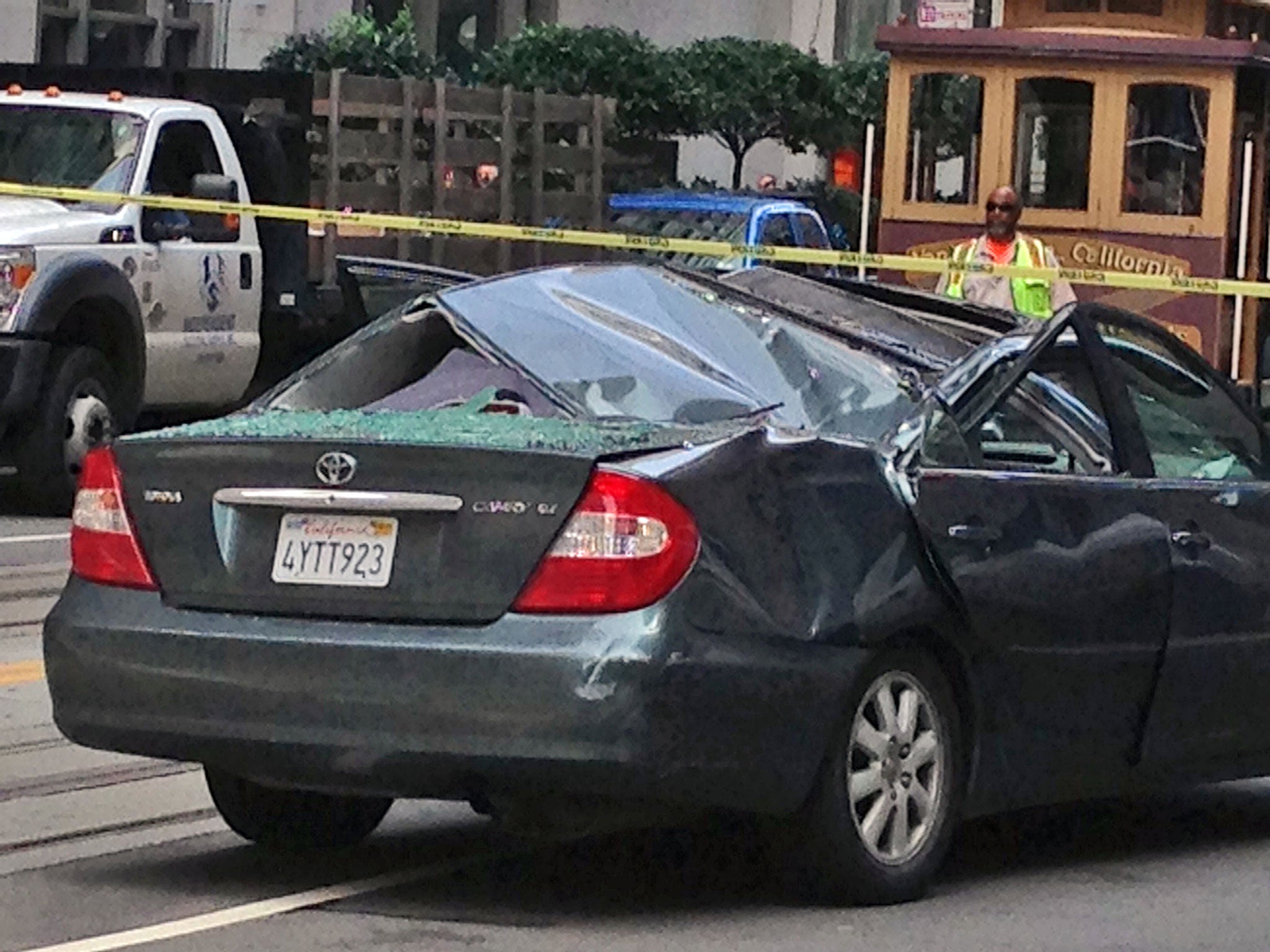 Police and citizens look over a car's caved in roof after a window washer fell 11 stories from the roof of a building and landed on the car