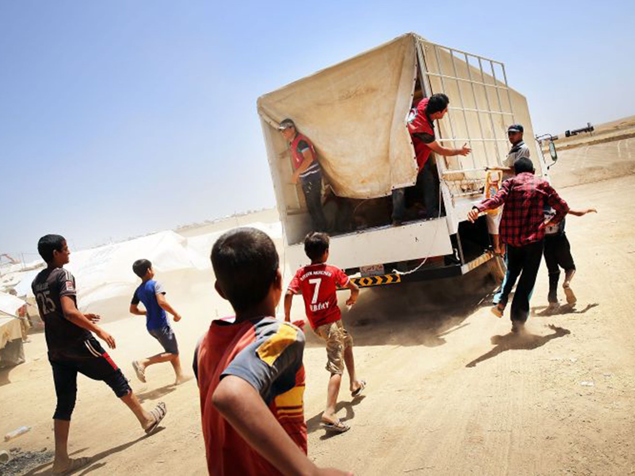 Iraqis at the Khazair camp for those caught up in the fighting around Mosul chase a Red Crescent truck delivering supplies