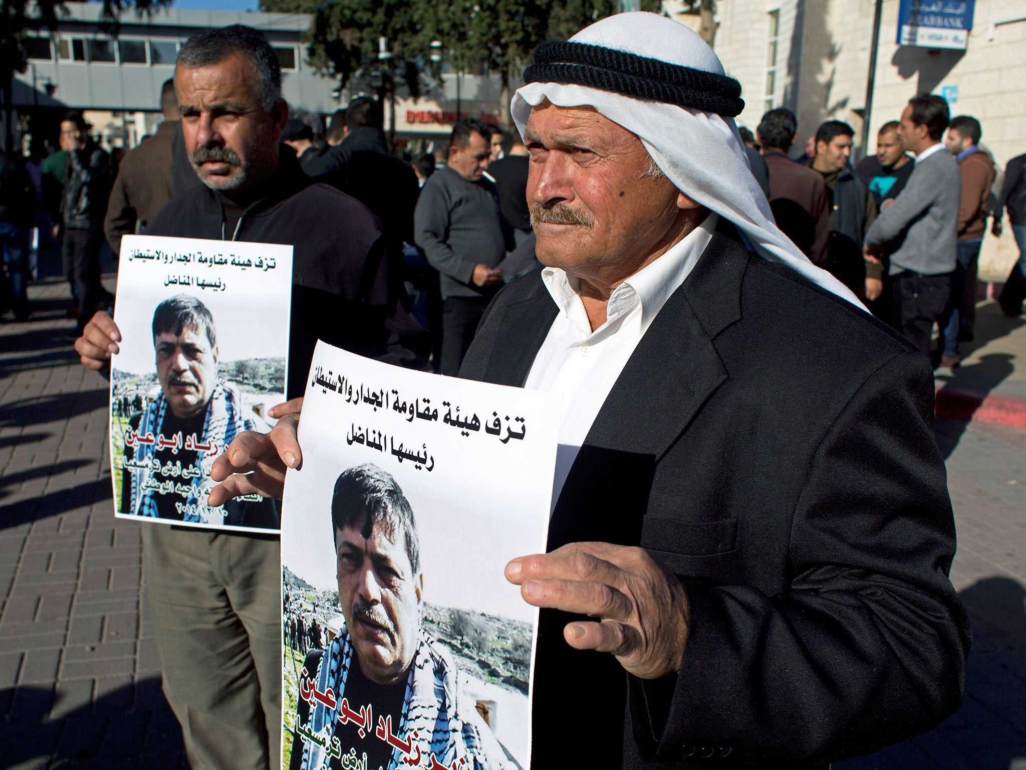 Mourners of Palestinian Cabinet member Ziad Abu Ain carry posters with his picture at the main hospital in the West Bank city of Ramallah