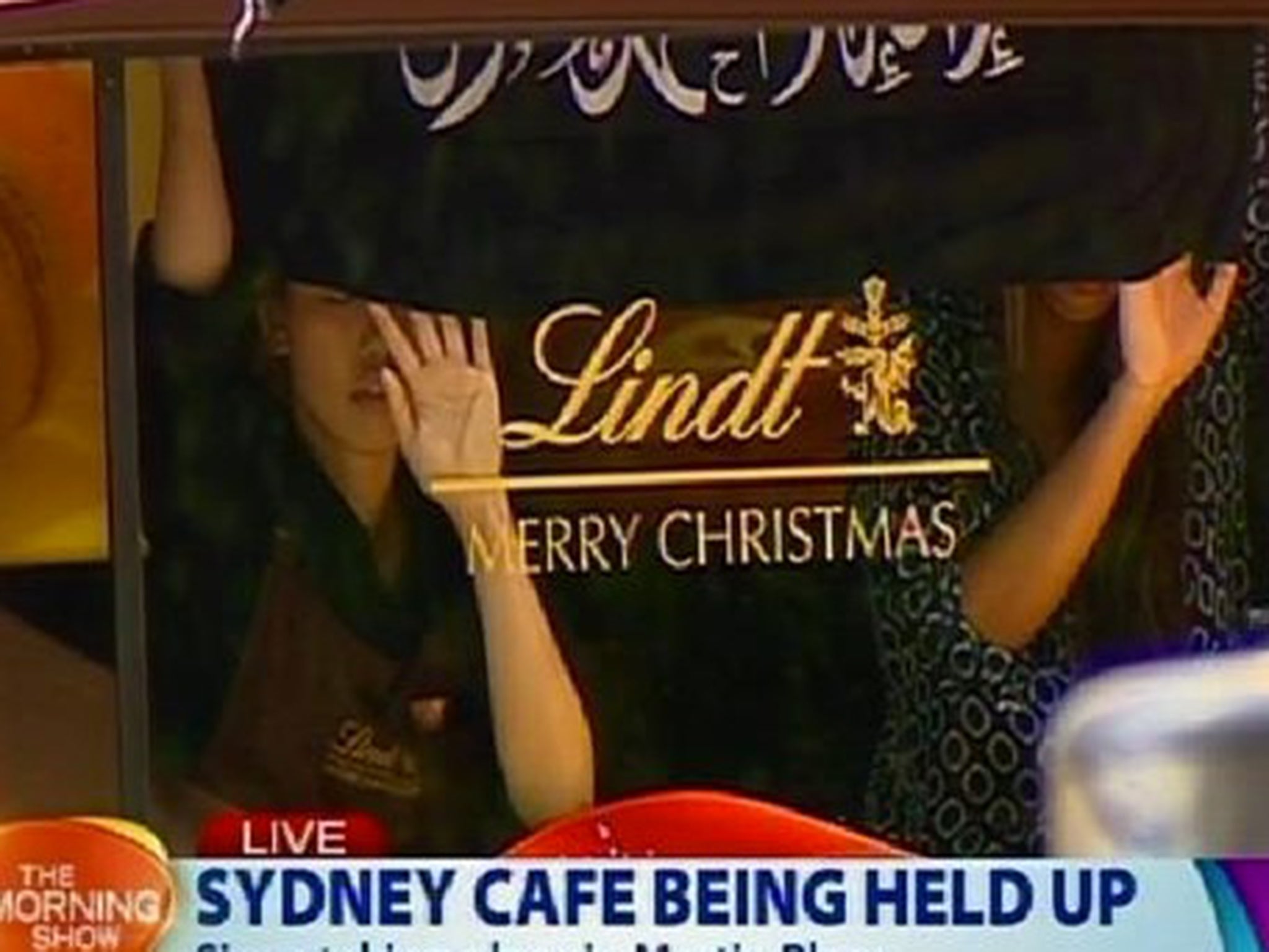 Two hostages hold up a black flag inscribed with Arabic writing at the window of the café in Sydney