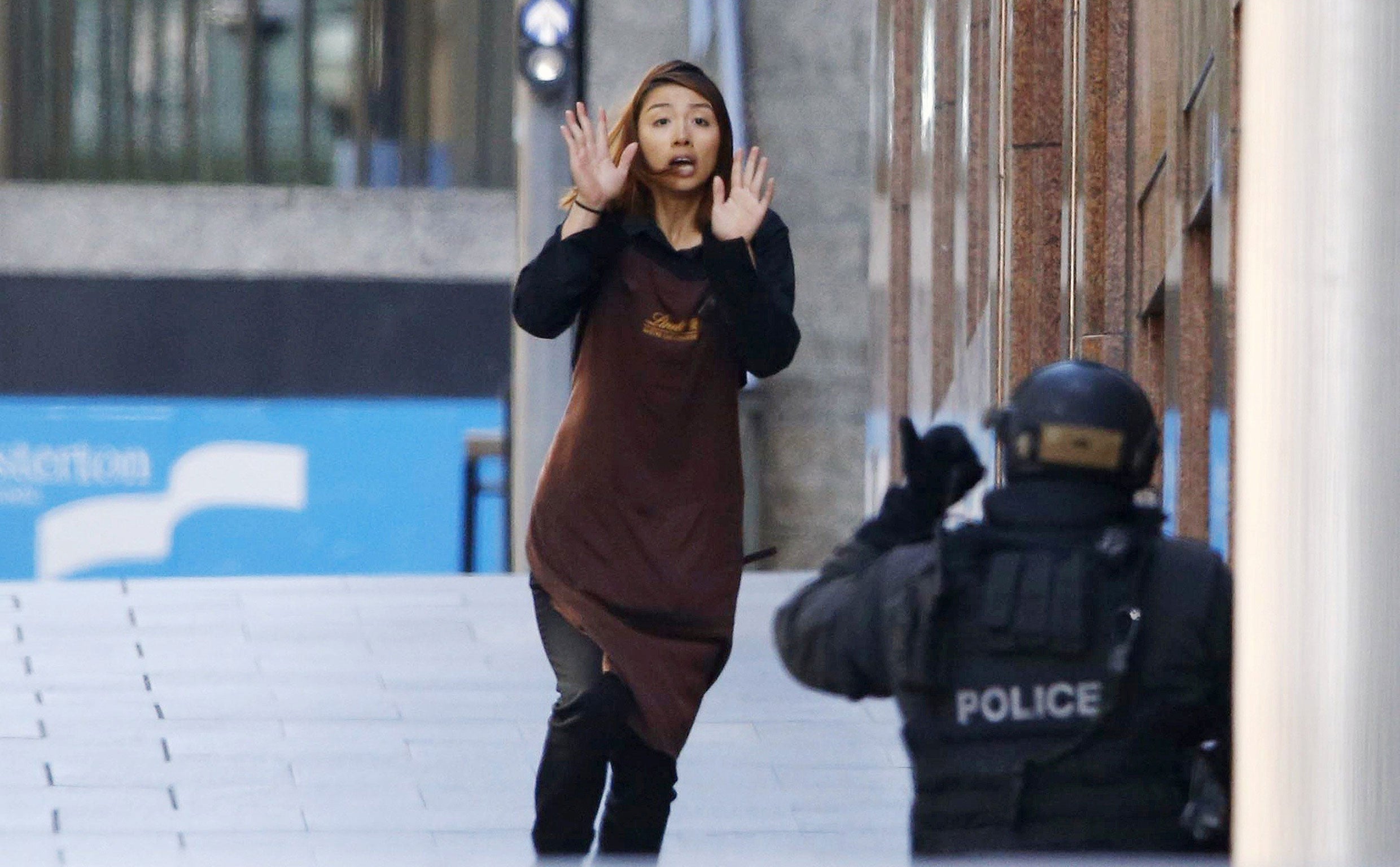 A hostage runs towards a police officer outside a cafe, where other hostages are being held, in Martin Place in central Sydney