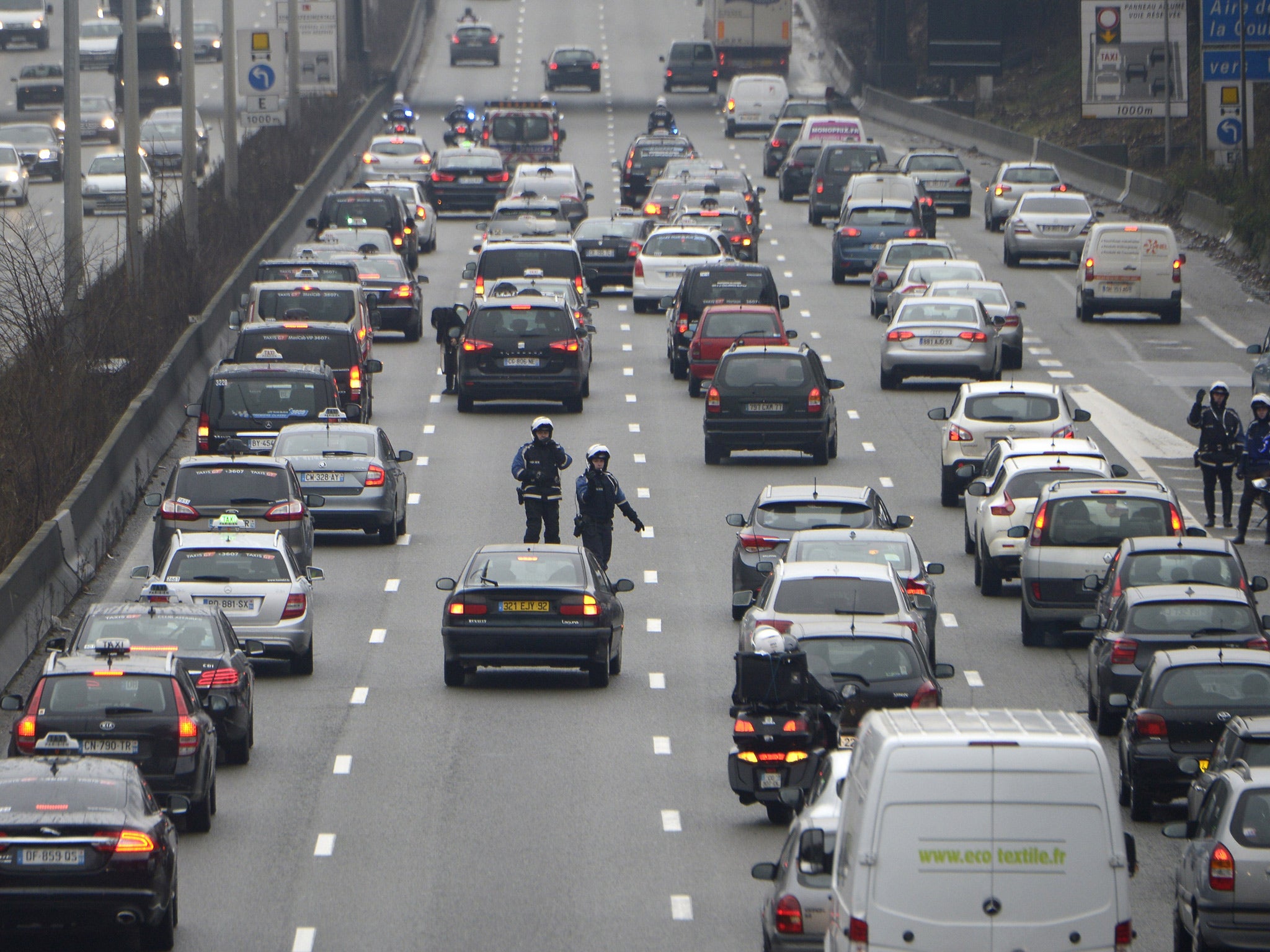 Policemen stand on the road as taxi drivers take part in a 'snail operation' on December 15, 2014 near Le Bourget, outside Paris