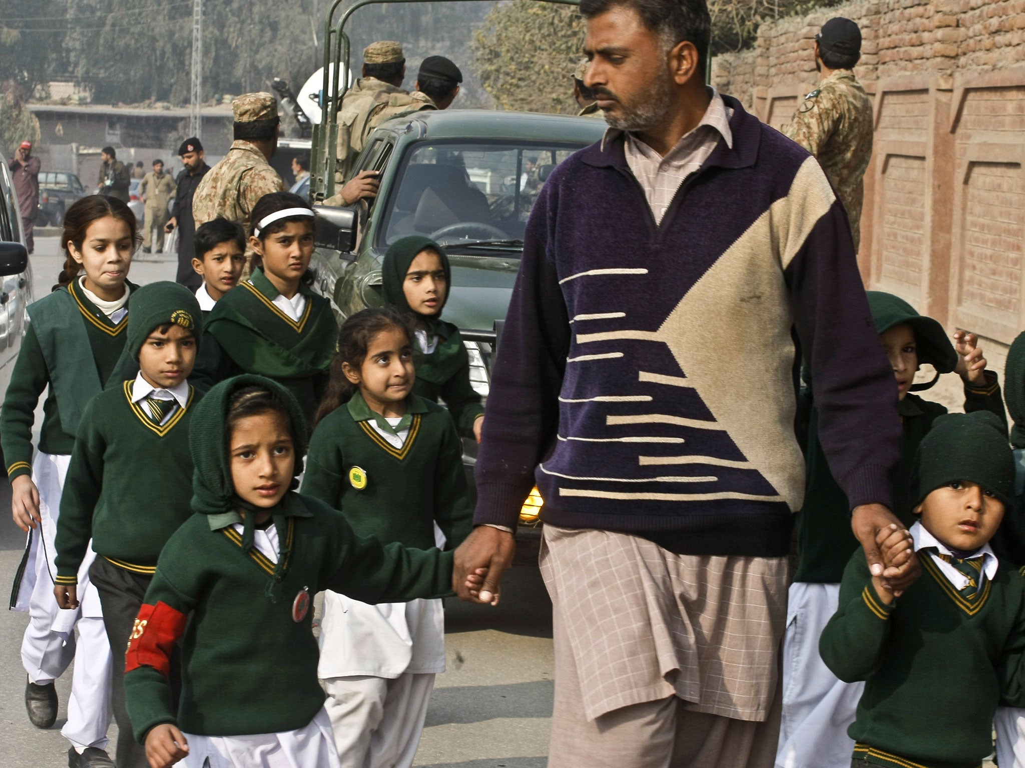 A plainclothes security officer escorts students rescued from nearby school during a Taliban attack in Peshawar