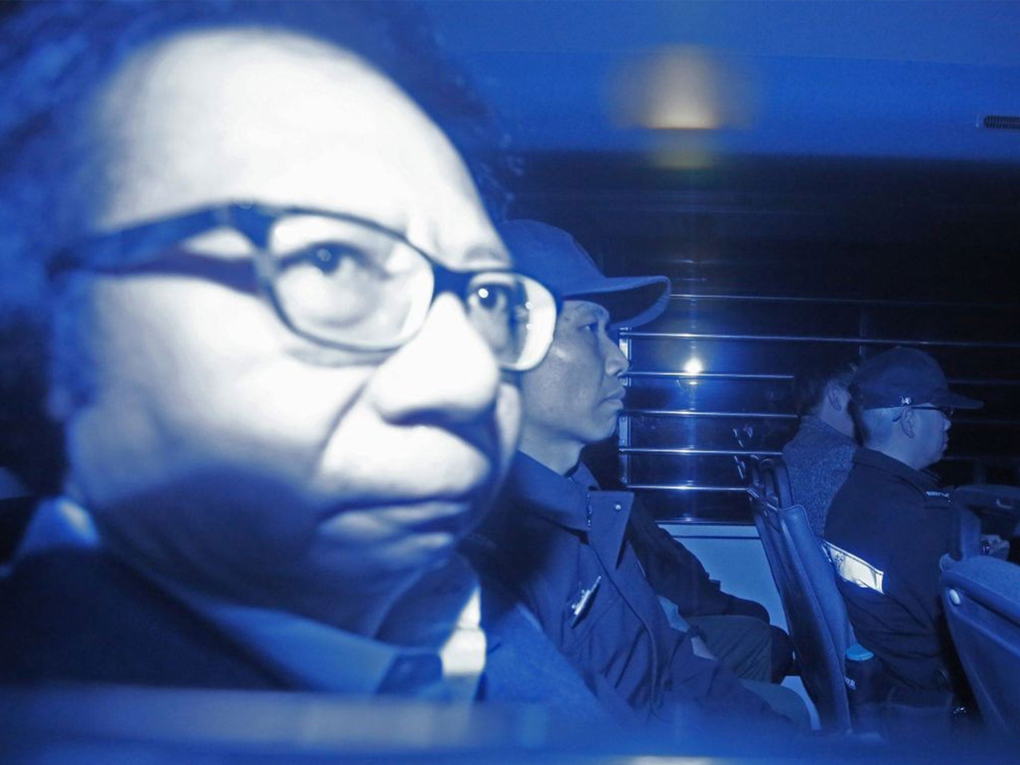 In this photo taken through a tinted glass, Thomas Kwok, left, co-chairman of Hong Kong developer Sun Hung Kai Properties, is escorted by staff members from Hong Kong Correctional Services inside a van outside the High Court in Hong Kong